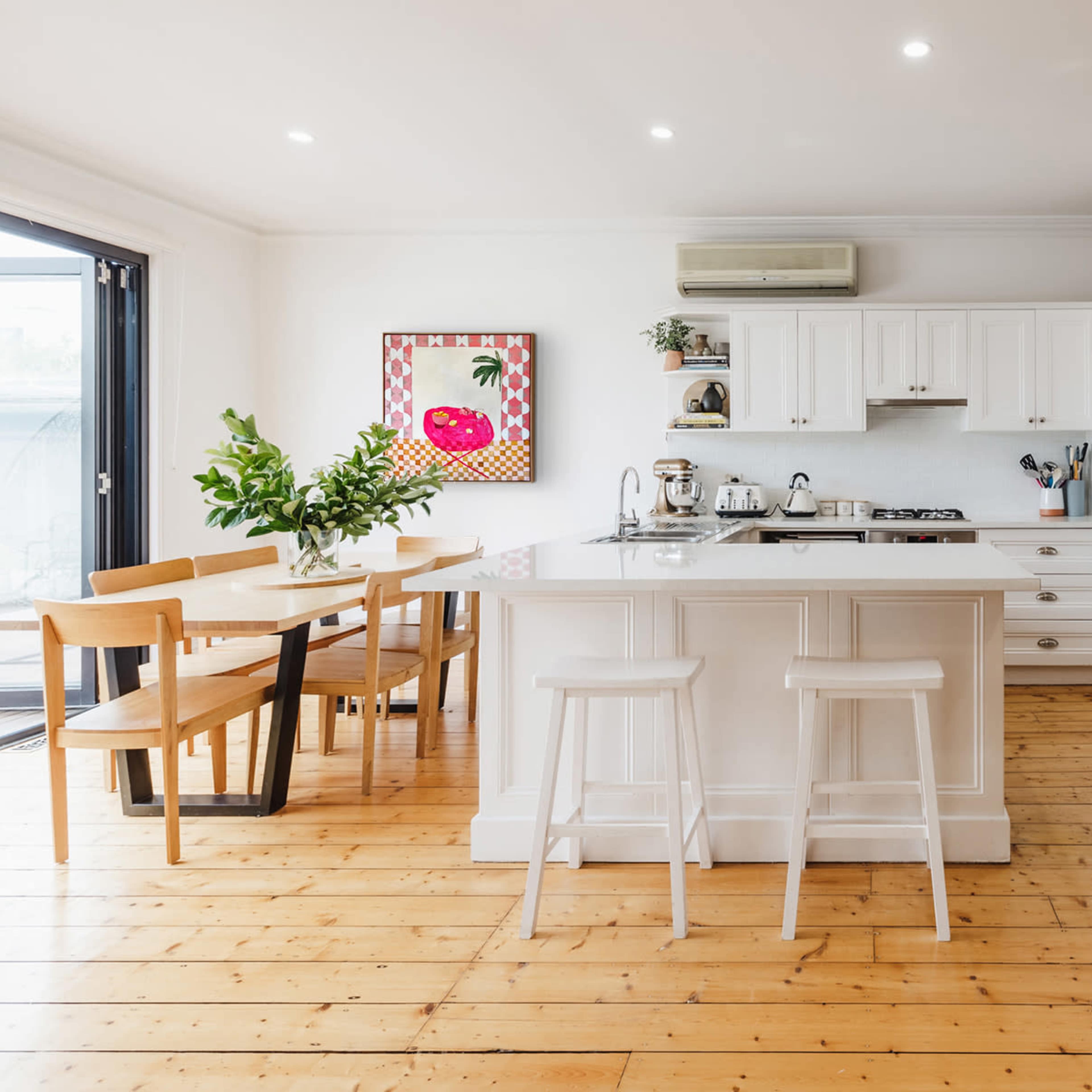 A modern kitchen features a central island, wooden flooring, and a dining area with a table and chairs.