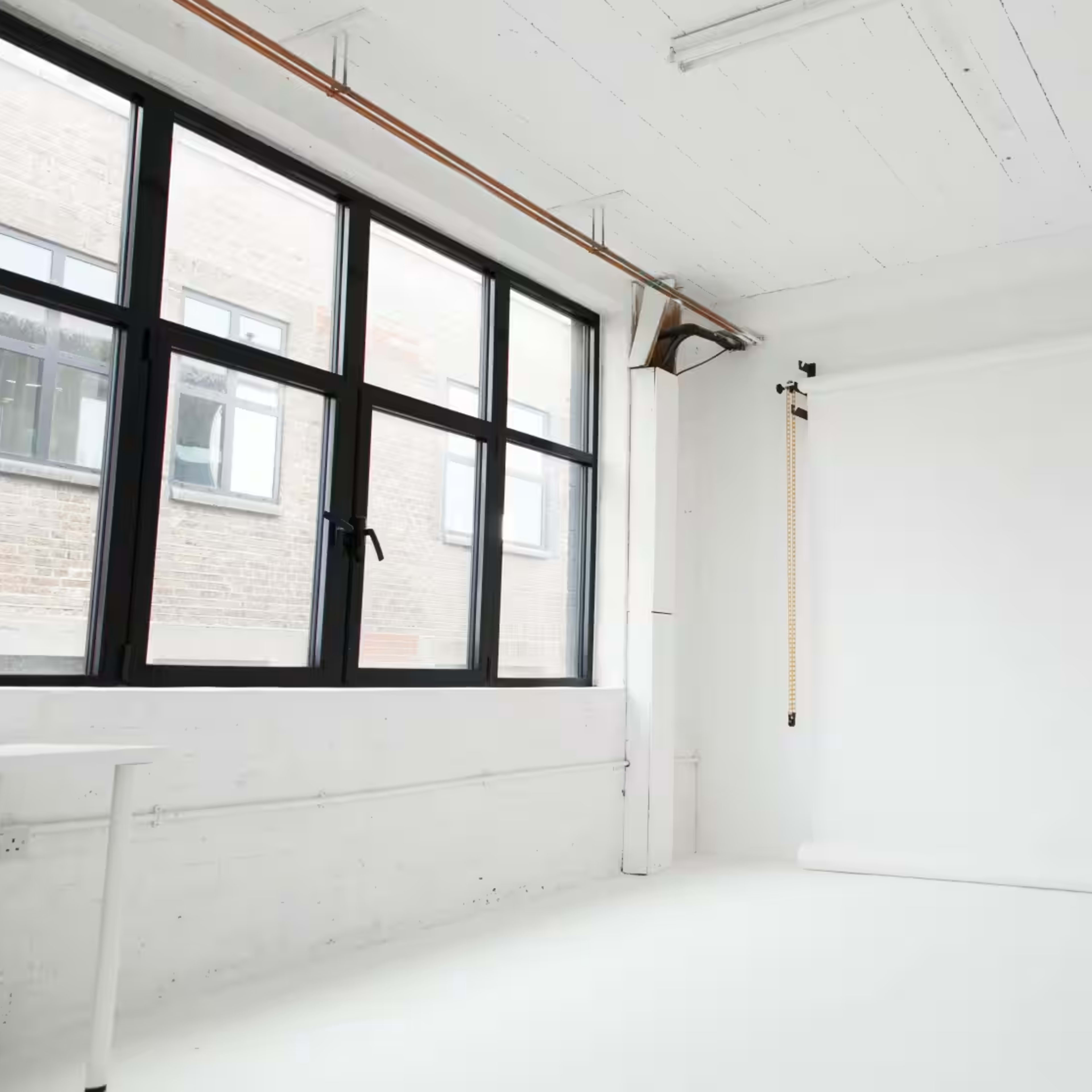 A bright, empty studio space with large windows and a white backdrop on a roll.