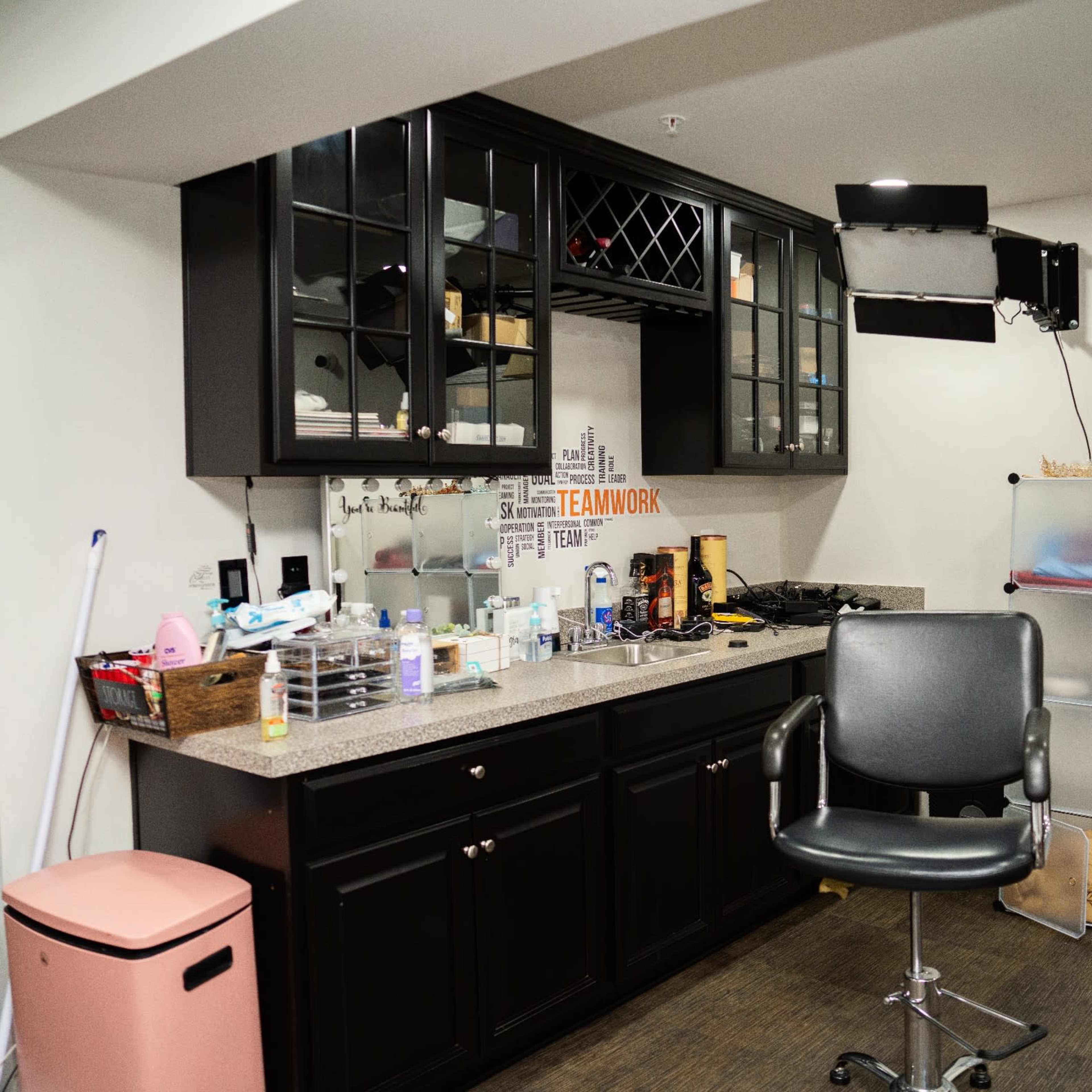 A small, well-organized salon space features a black cabinet, a salon chair, and various beauty products on the counter.