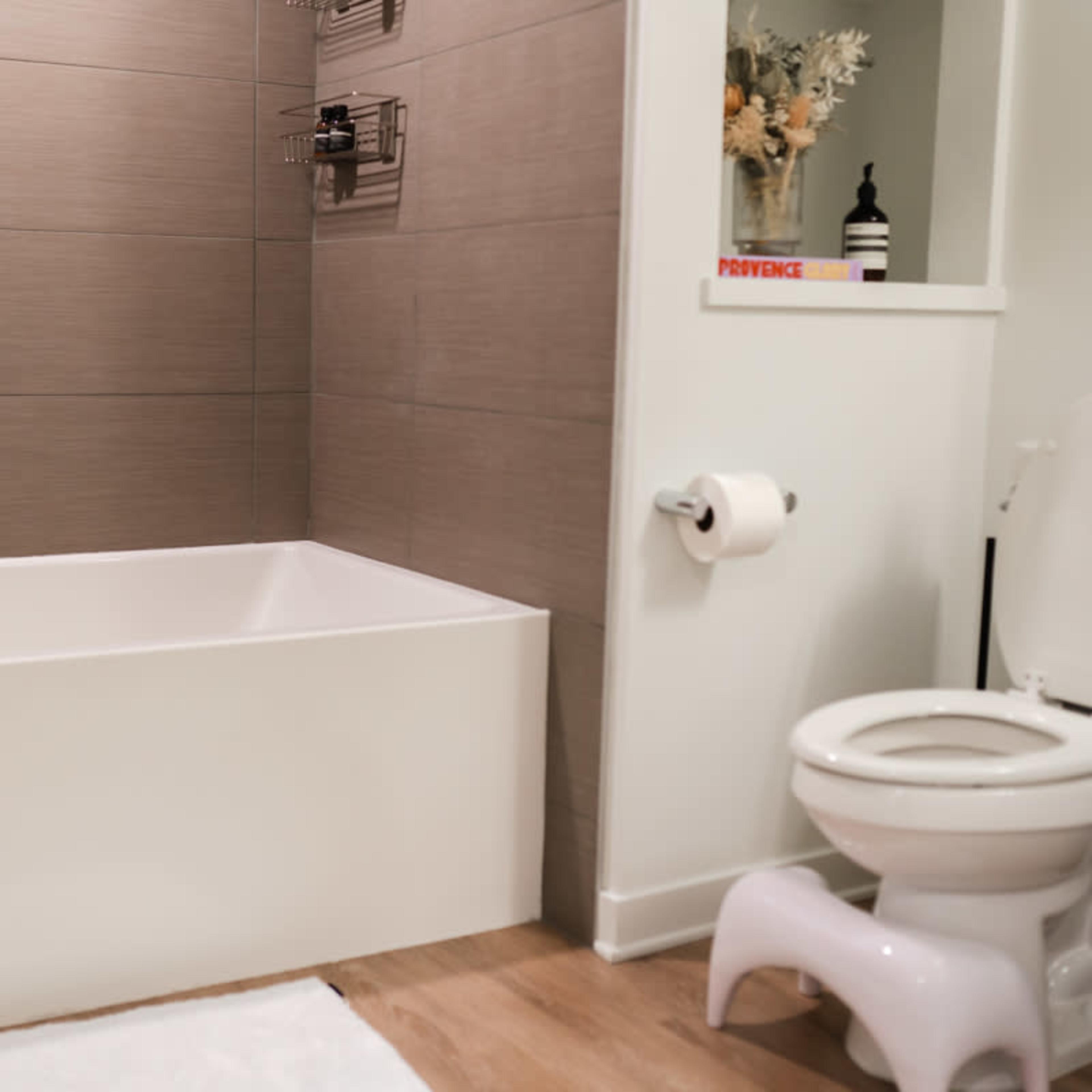 A bathroom with a tub, toilet, and a small shelf holding decorative items.