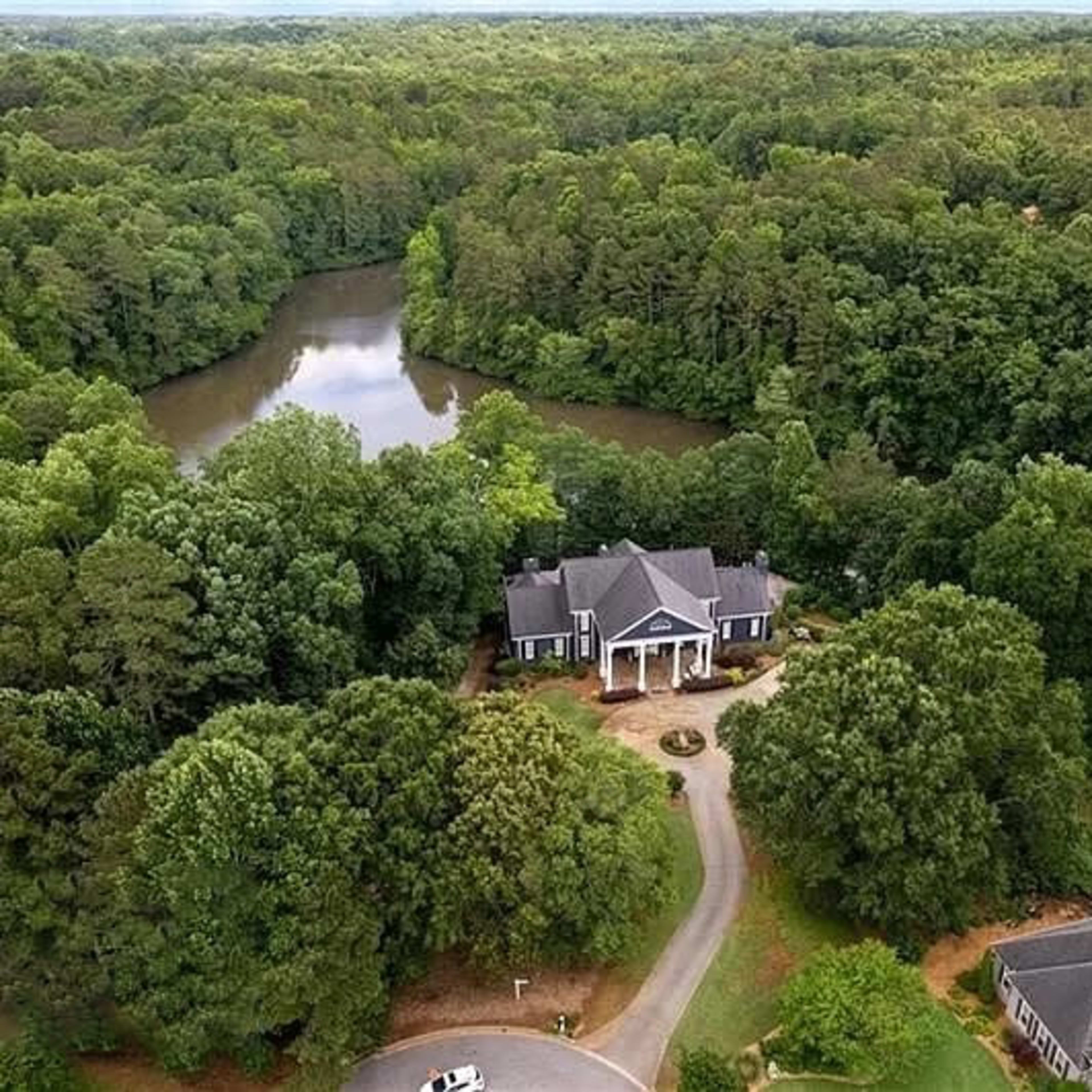 A large house surrounded by dense greenery and a winding river in the background.