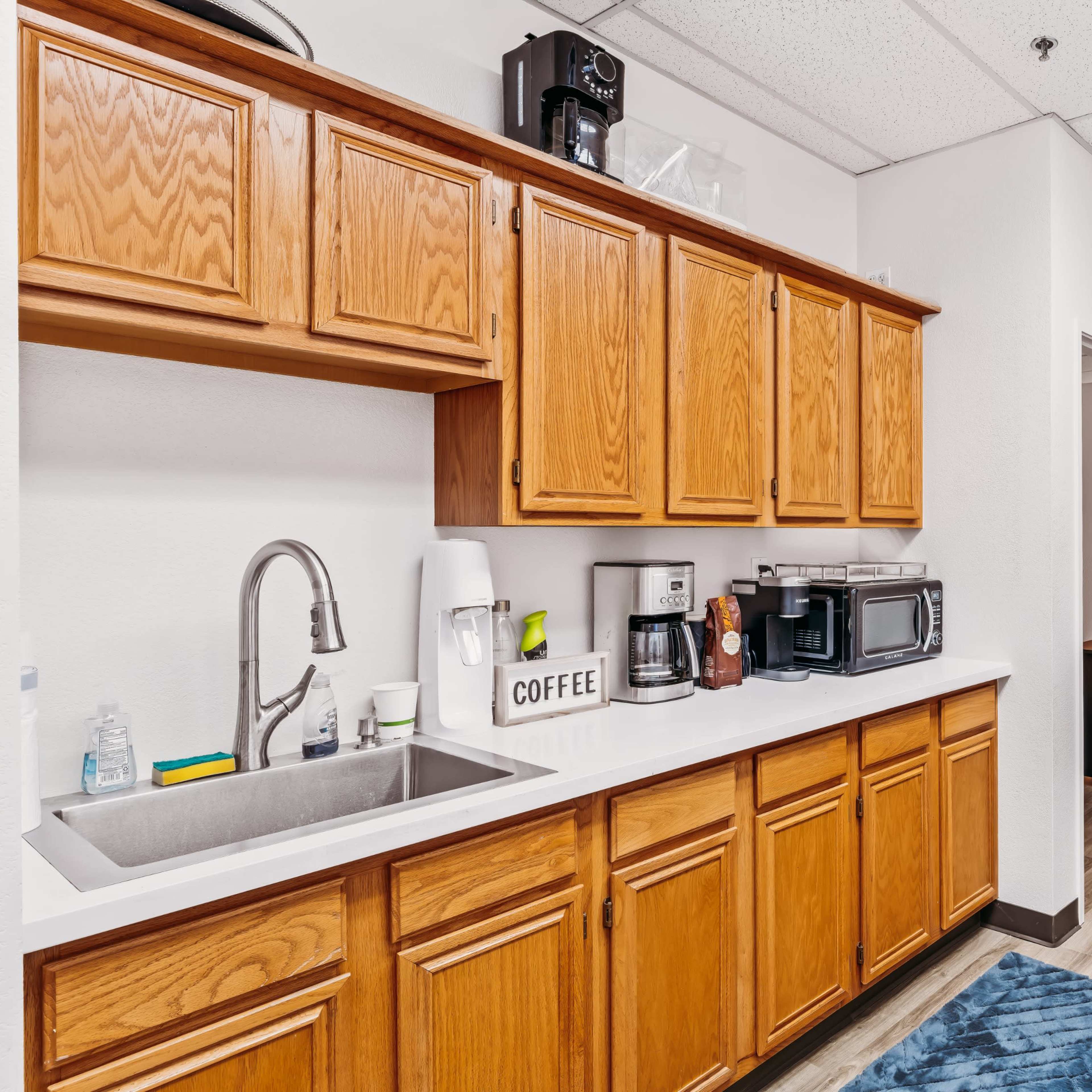 A modern kitchen area with wooden cabinets, a sink, various kitchen appliances, and a door leading to another room.
