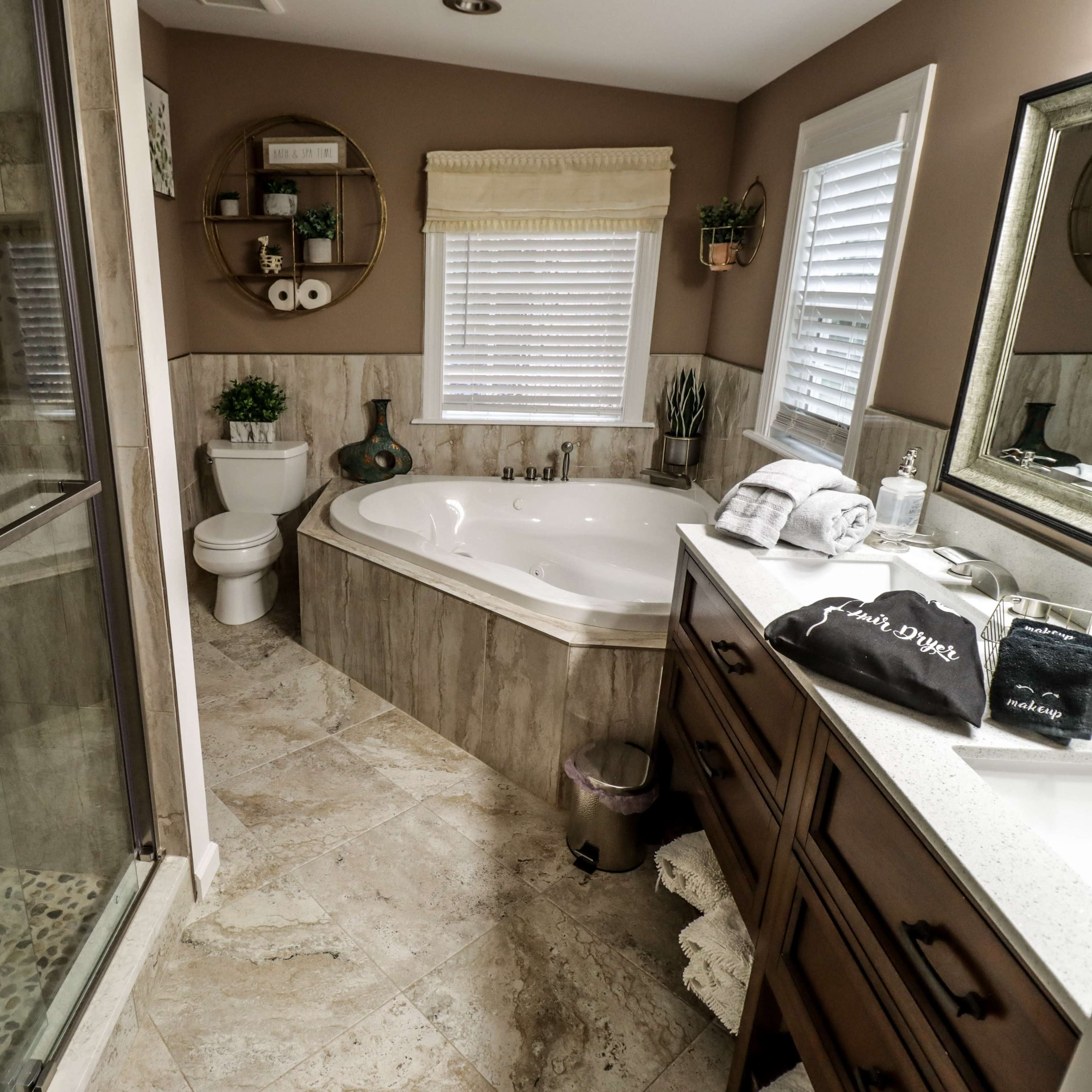 A modern bathroom featuring a glass shower enclosure, a large soaking tub, a double-sink vanity, and neutral-colored walls.