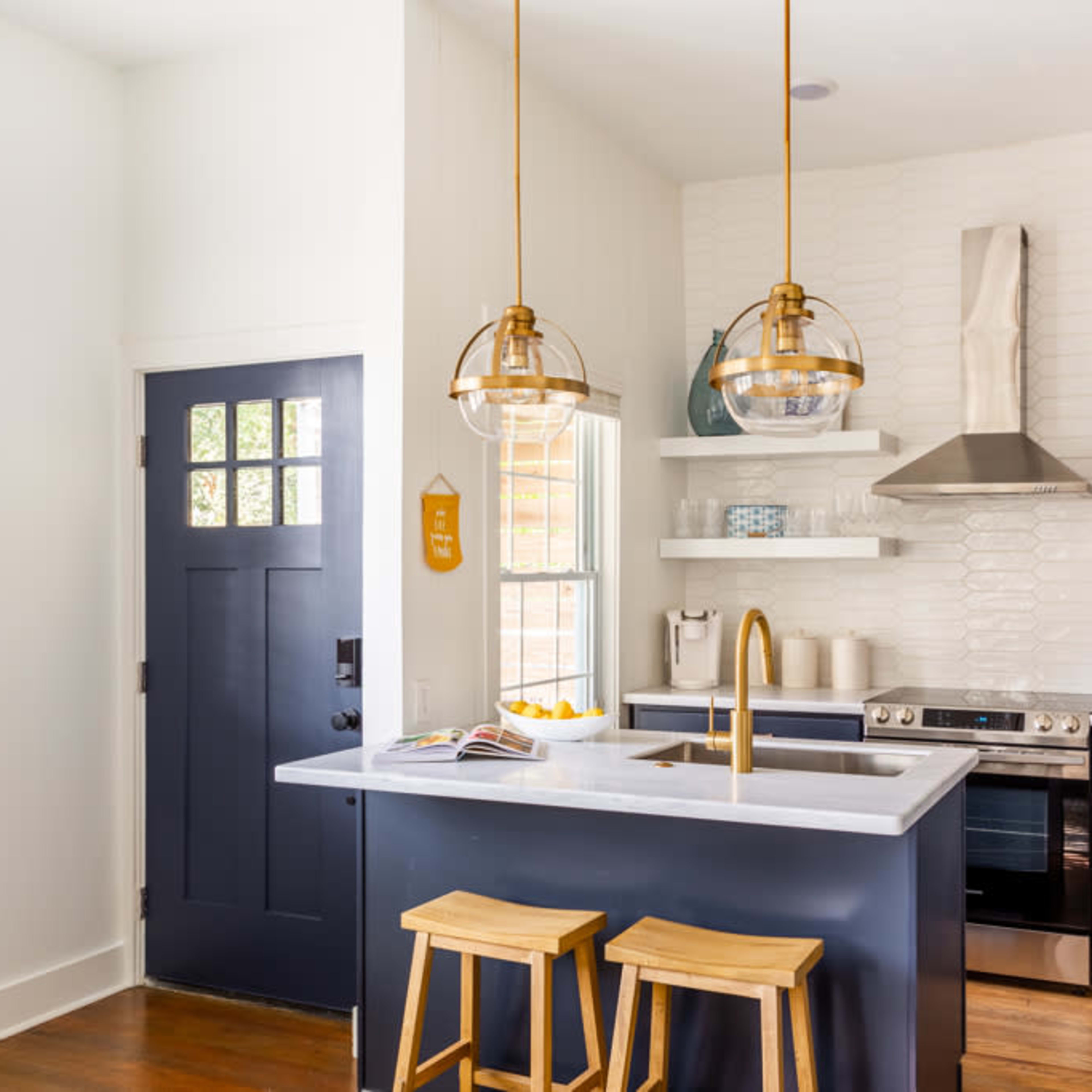 A modern kitchen features blue cabinetry, a large island with bar stools, and gold pendant lights above the sink, alongside stainless steel appliances.