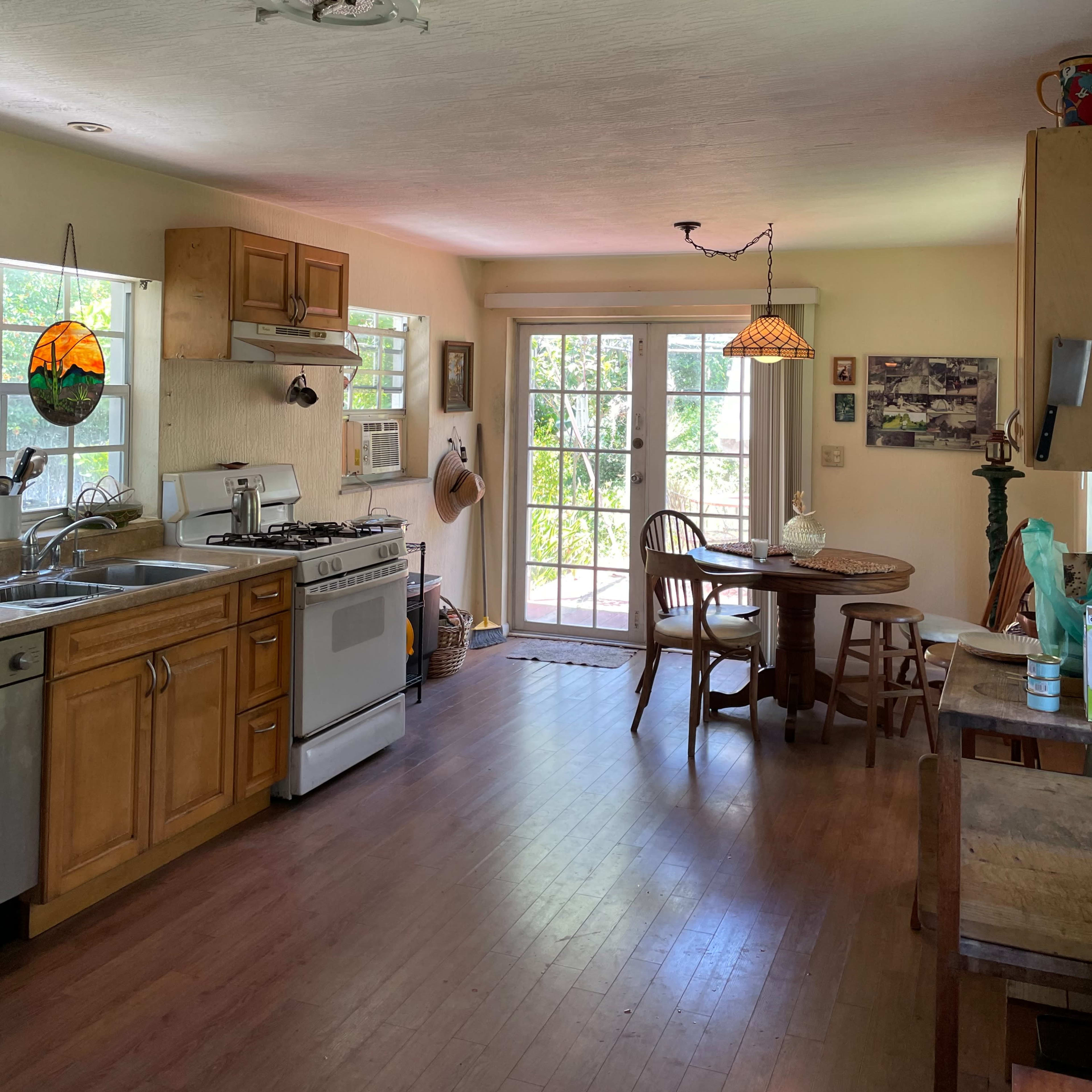 The kitchen features wooden cabinets, a gas stove, and a dining table near a glass door that opens to the outside.