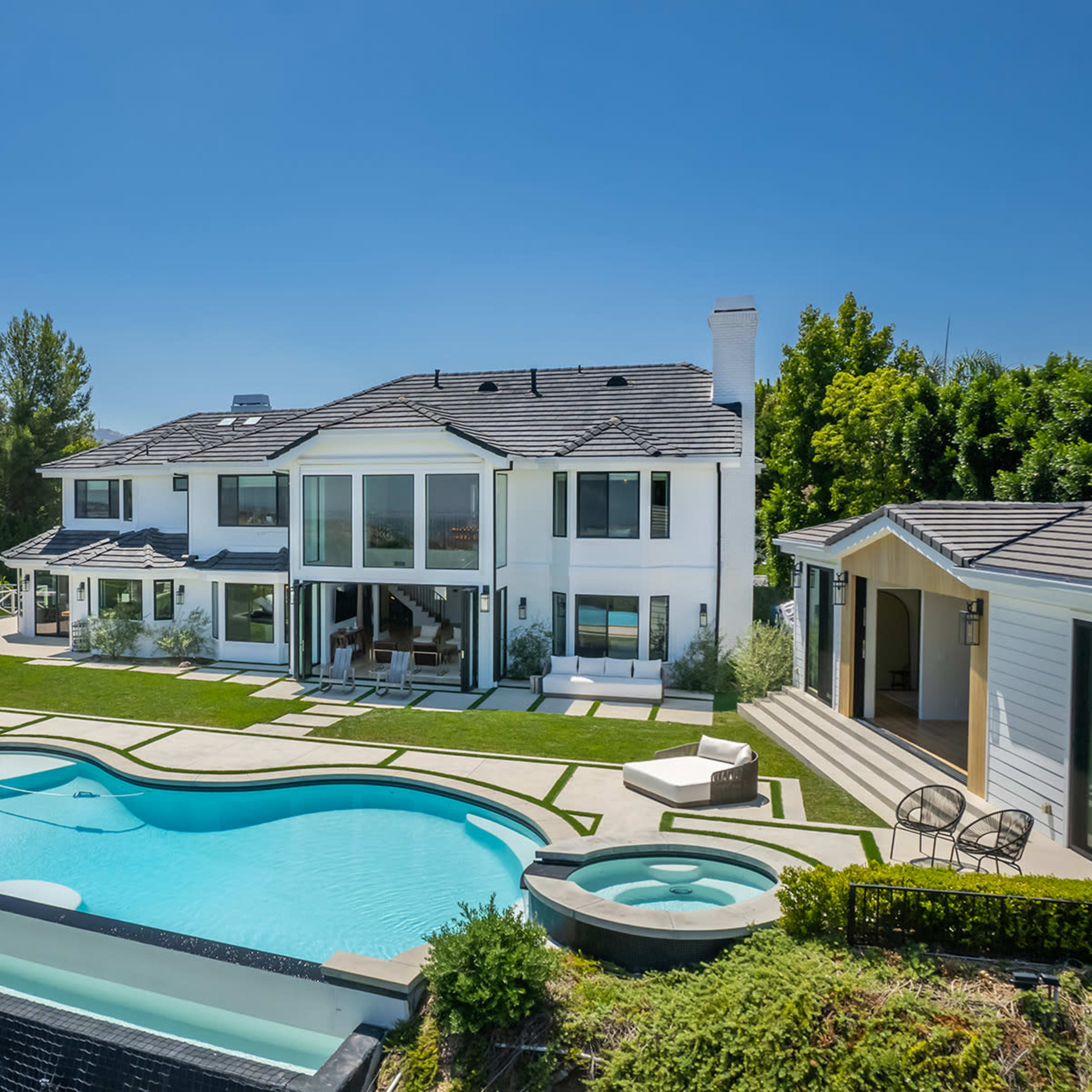 A modern two-story white house with large windows, a swimming pool, and landscaped outdoor areas featuring lounge chairs and a gazebo.