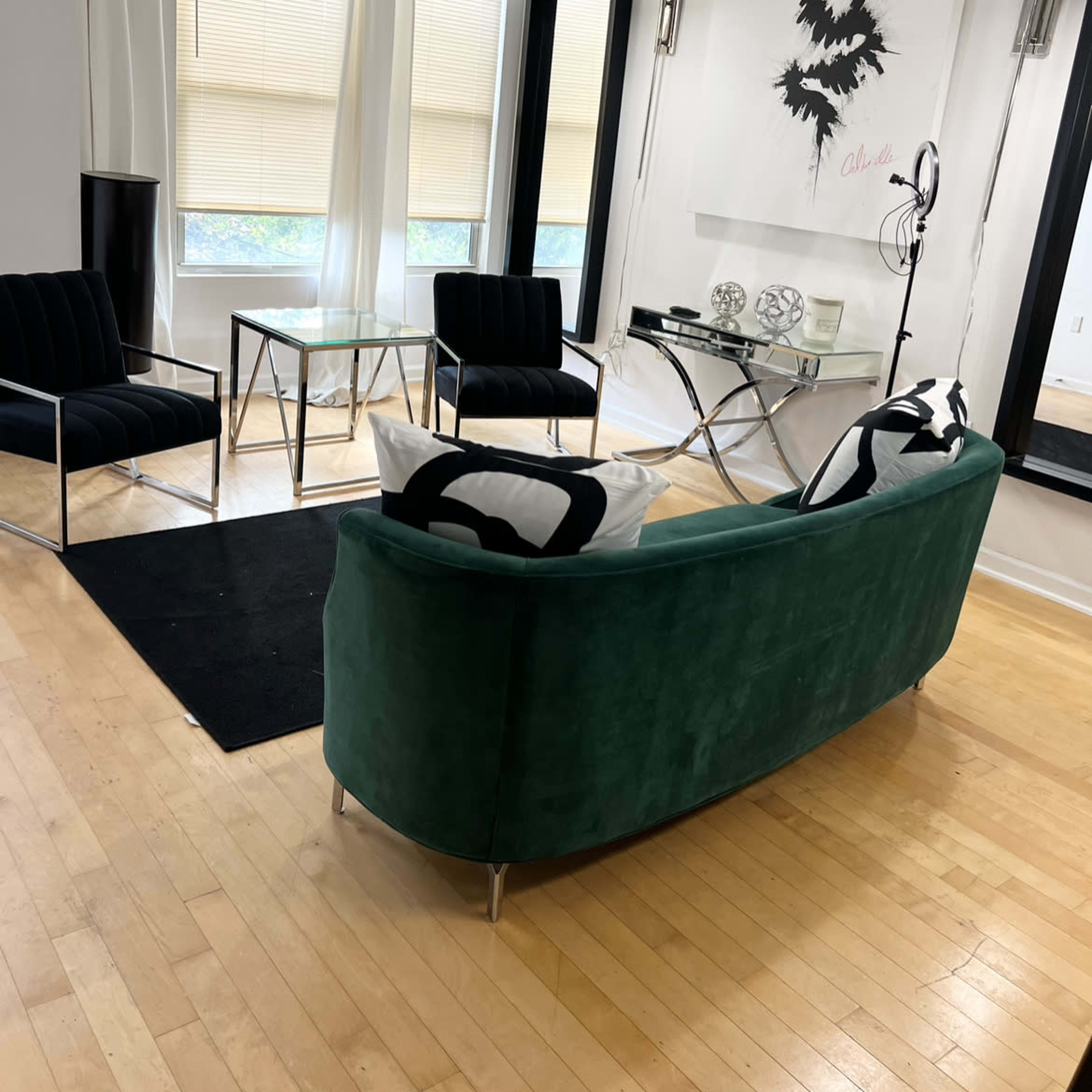 A modern living room with a green curved sofa, two black armchairs, a glass coffee table, and abstract wall art.