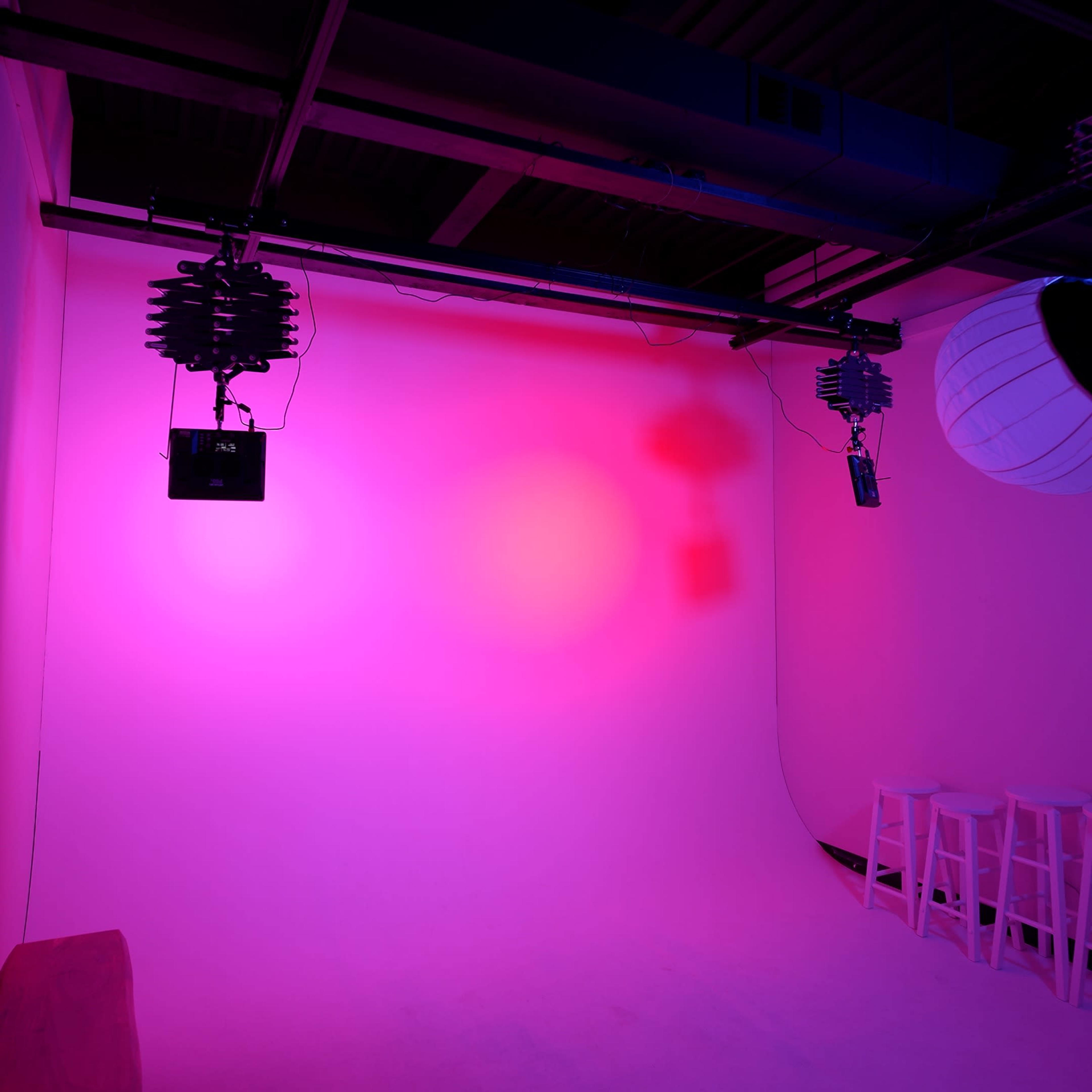 A studio space with pink lighting, featuring a seamless backdrop and mounted lighting equipment.