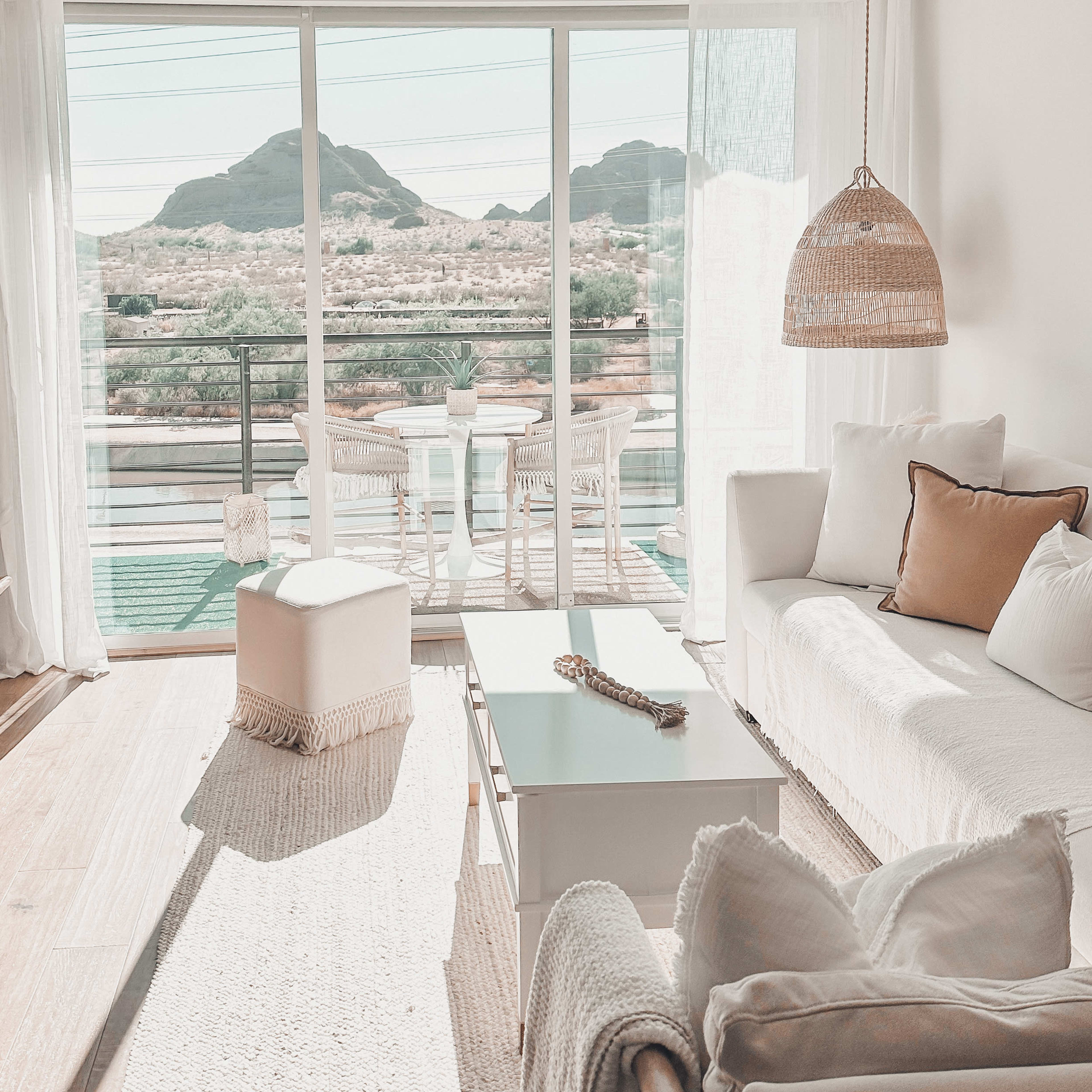 A bright living room with a white sofa, coffee table, and a view of mountains through sliding glass doors leading to a small outdoor seating area.