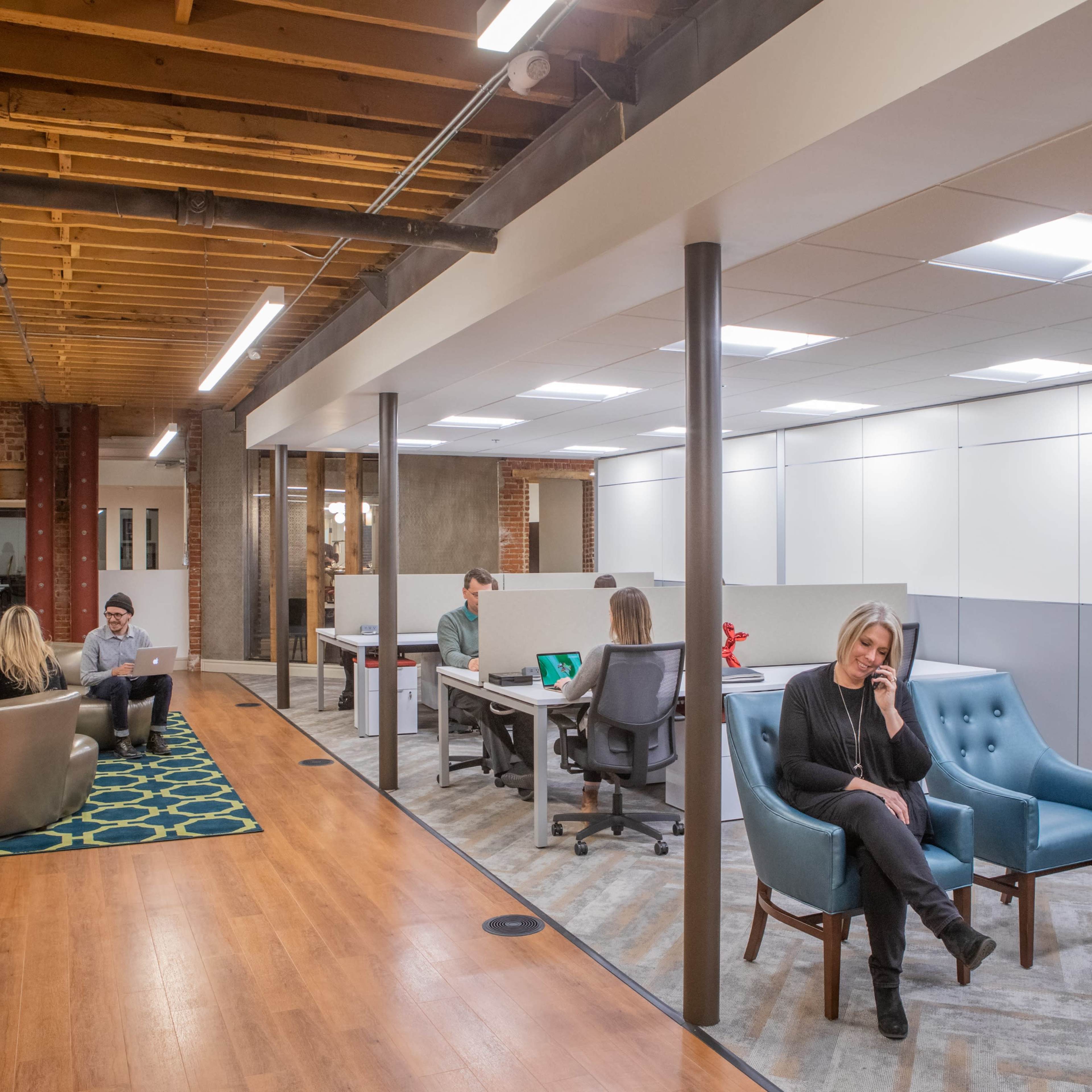 A modern office space with different areas for work and relaxation, featuring a lounge with sofas and a group of people at desks.