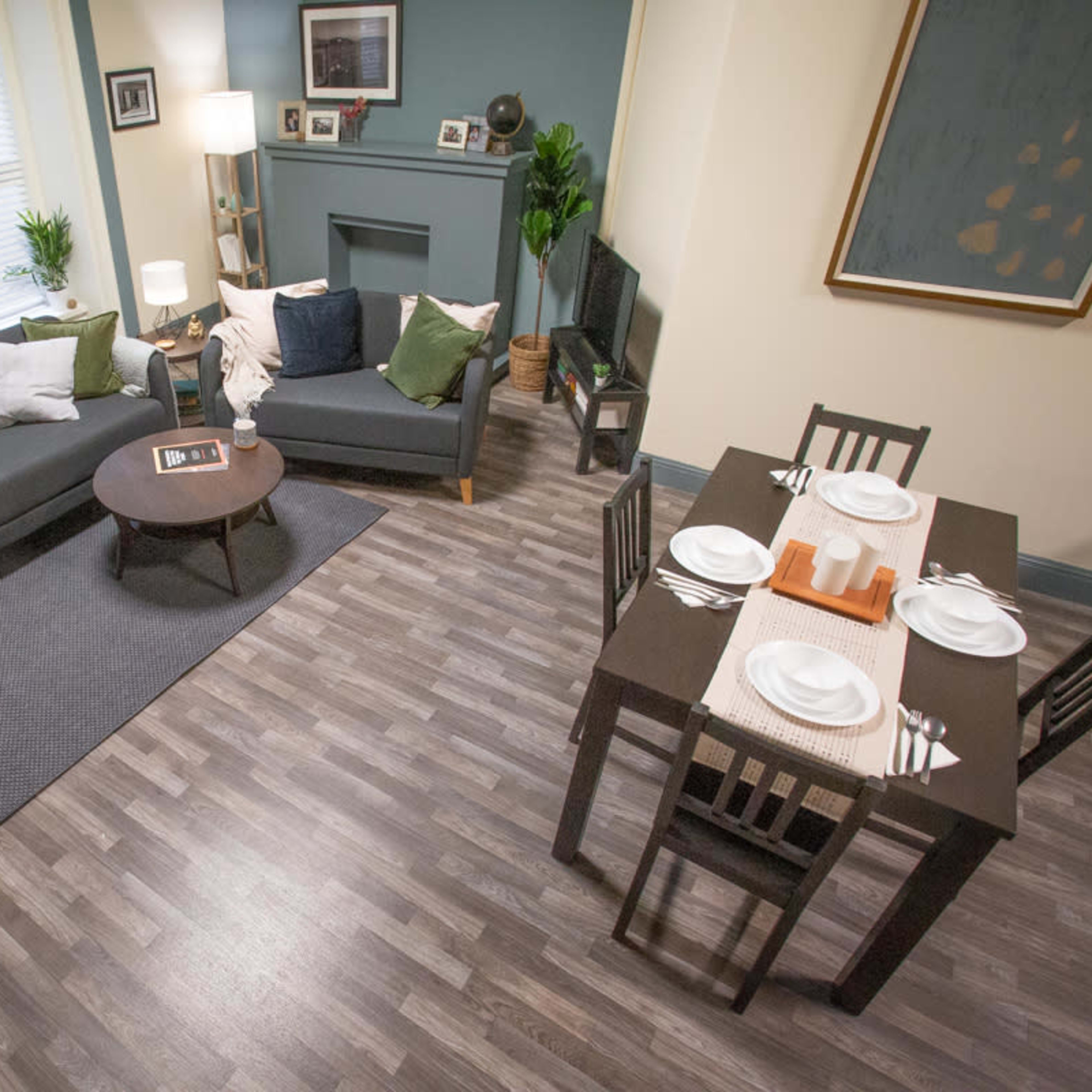 A decorated living room with a sofa, armchair, coffee table, and a dining table set for a meal, all situated on laminate flooring.