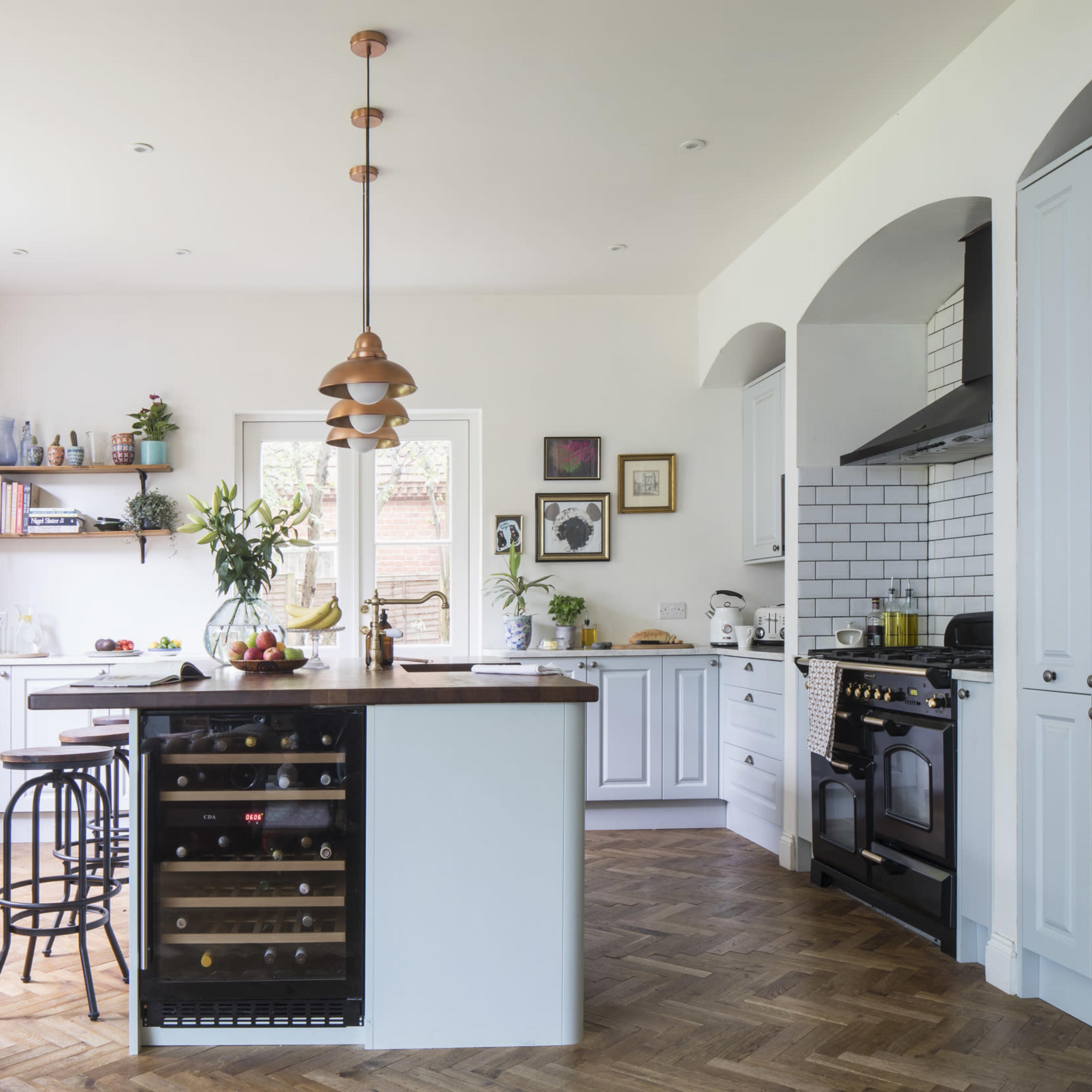 A modern kitchen features white cabinetry, a central island with a wine cooler, and large windows that allow natural light to fill the space.
