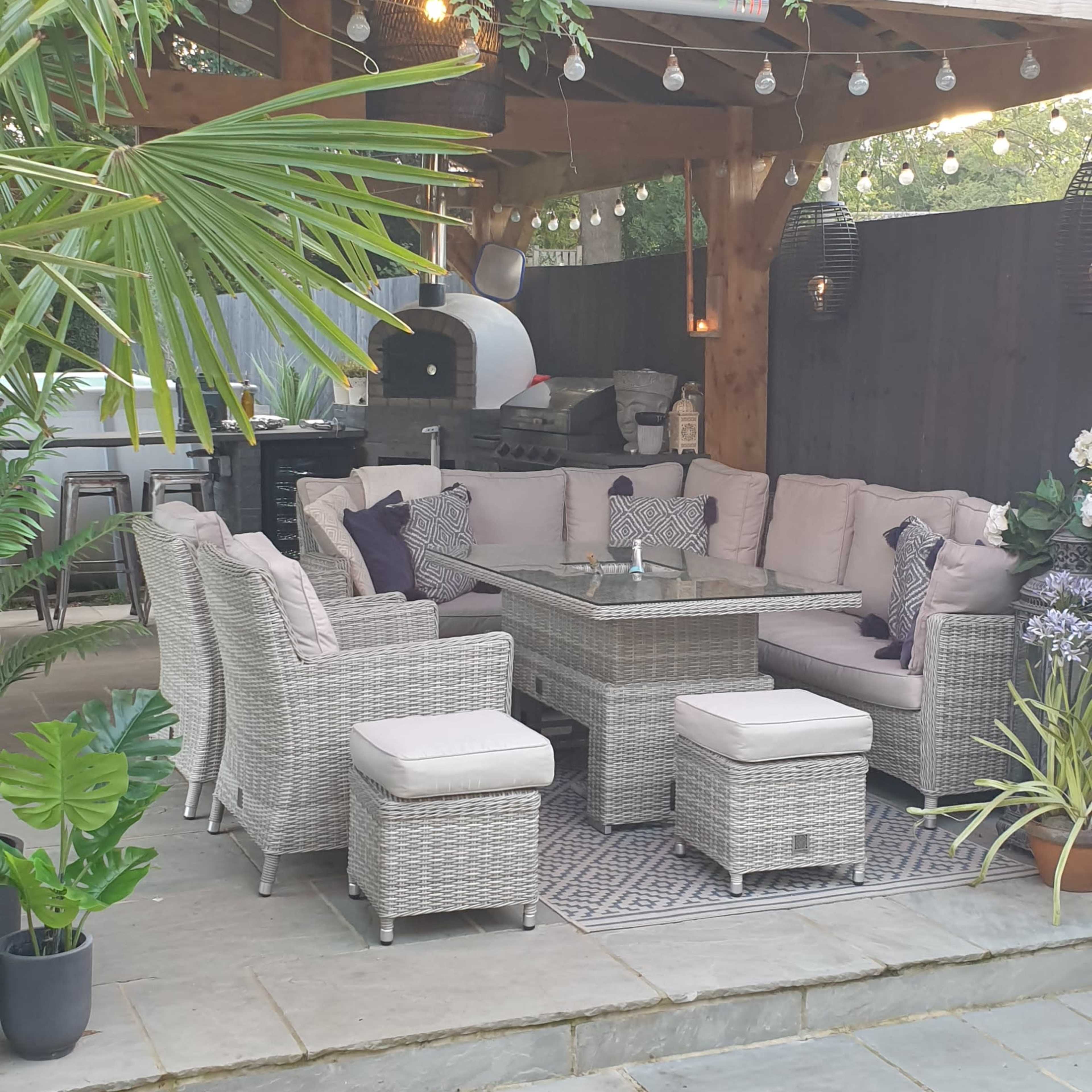 A covered outdoor seating area with a large sectional couch, a coffee table, and decorative plants, illuminated by string lights.