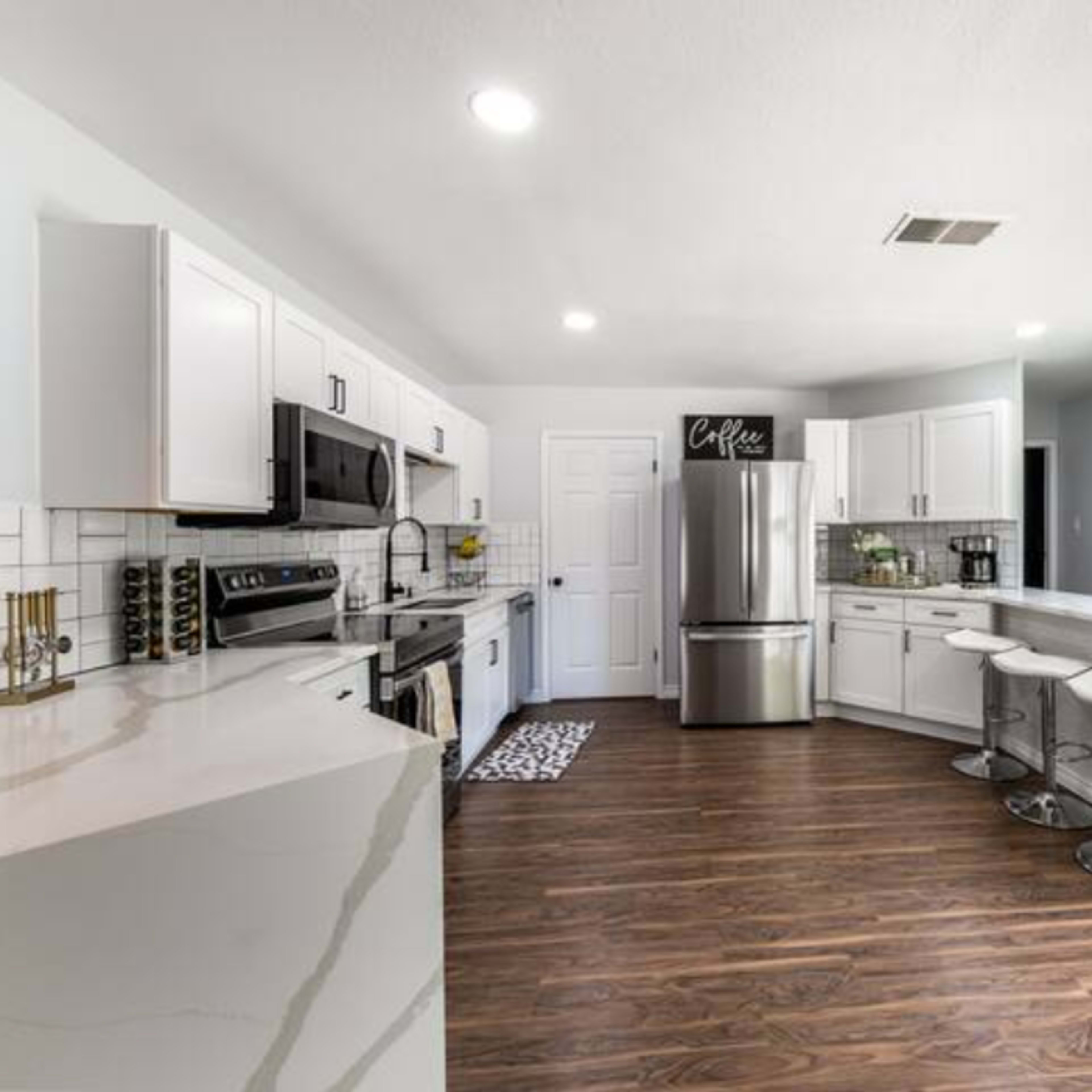 A modern kitchen features stainless steel appliances, white cabinetry, and a bar with three stools.