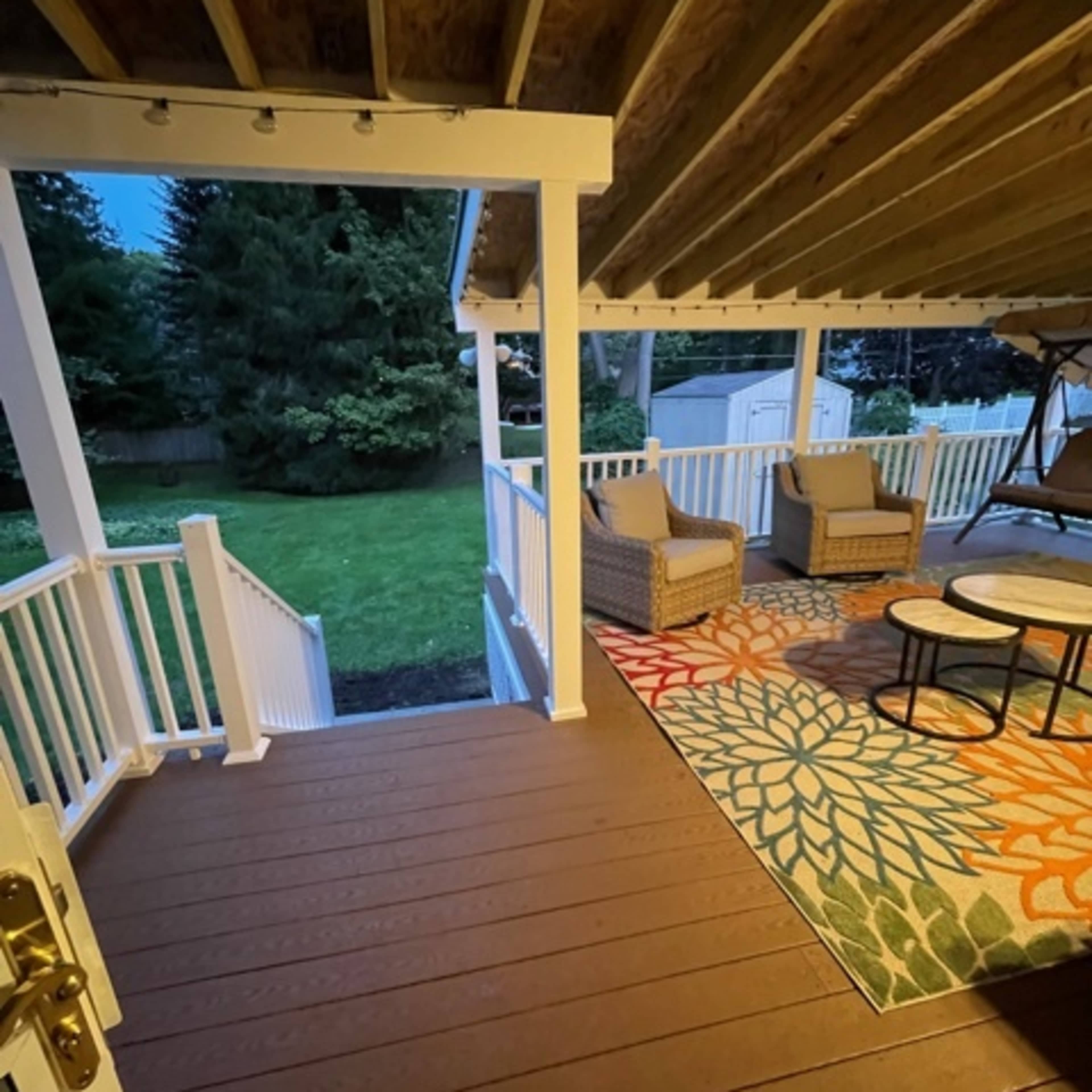 A porch with two chairs and a table, overlooking a grassy backyard at dusk.