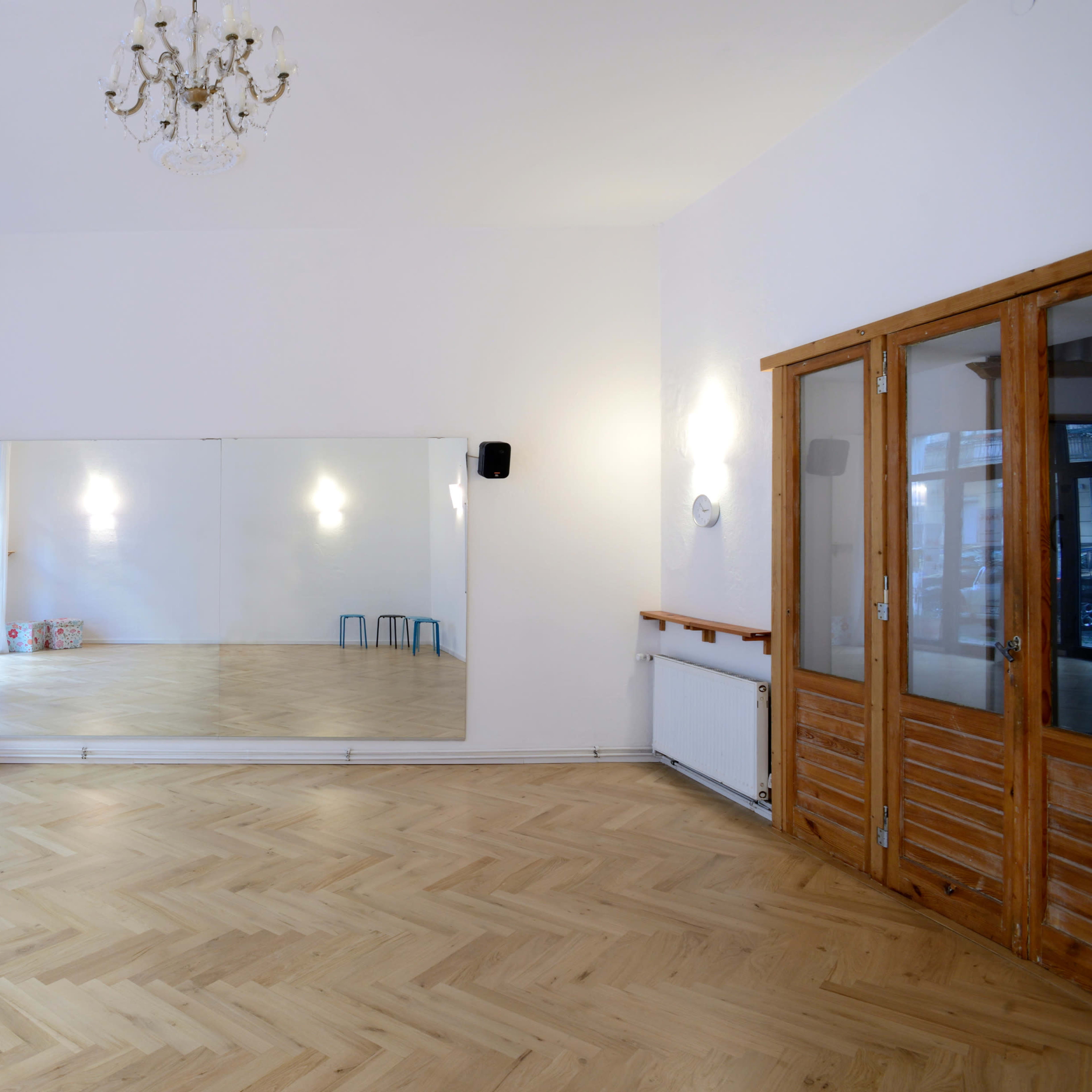 A spacious, empty room with a large mirror on one wall, wooden flooring, and a set of wooden double doors.