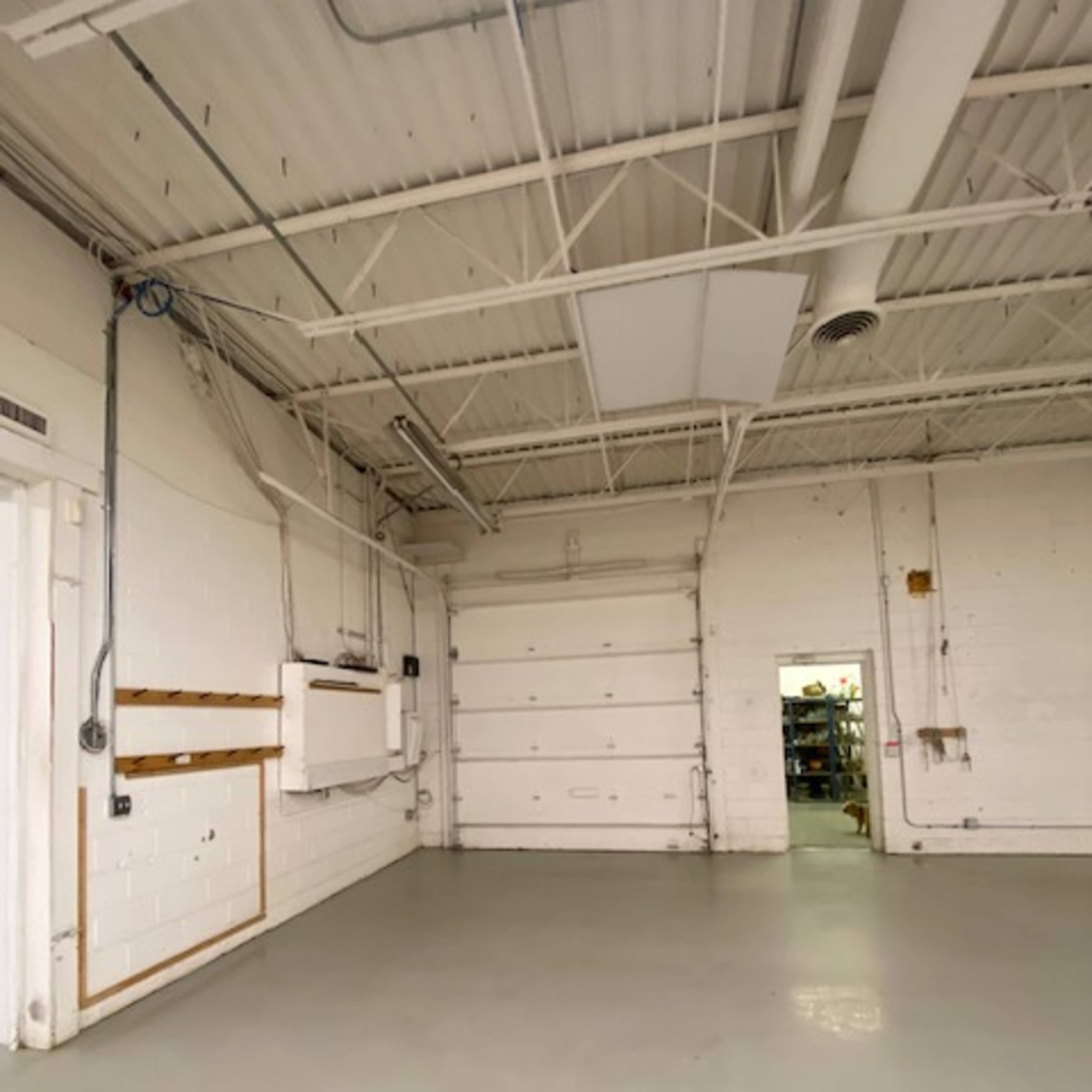 An empty industrial space features white walls, a concrete floor, and a large garage door.