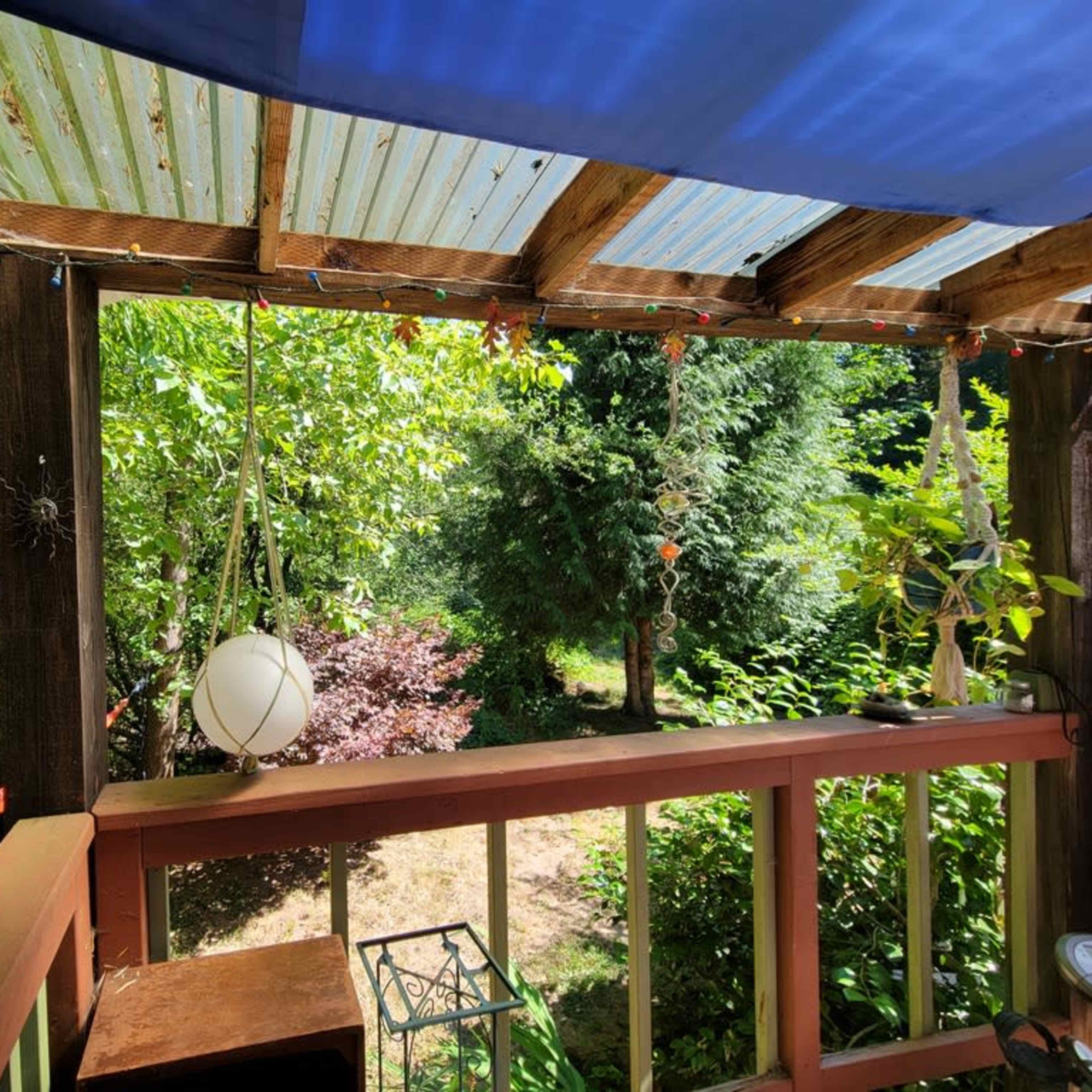 A wooden porch overlooks a garden filled with lush greenery and decorative elements, including hanging plants and a light fixture.