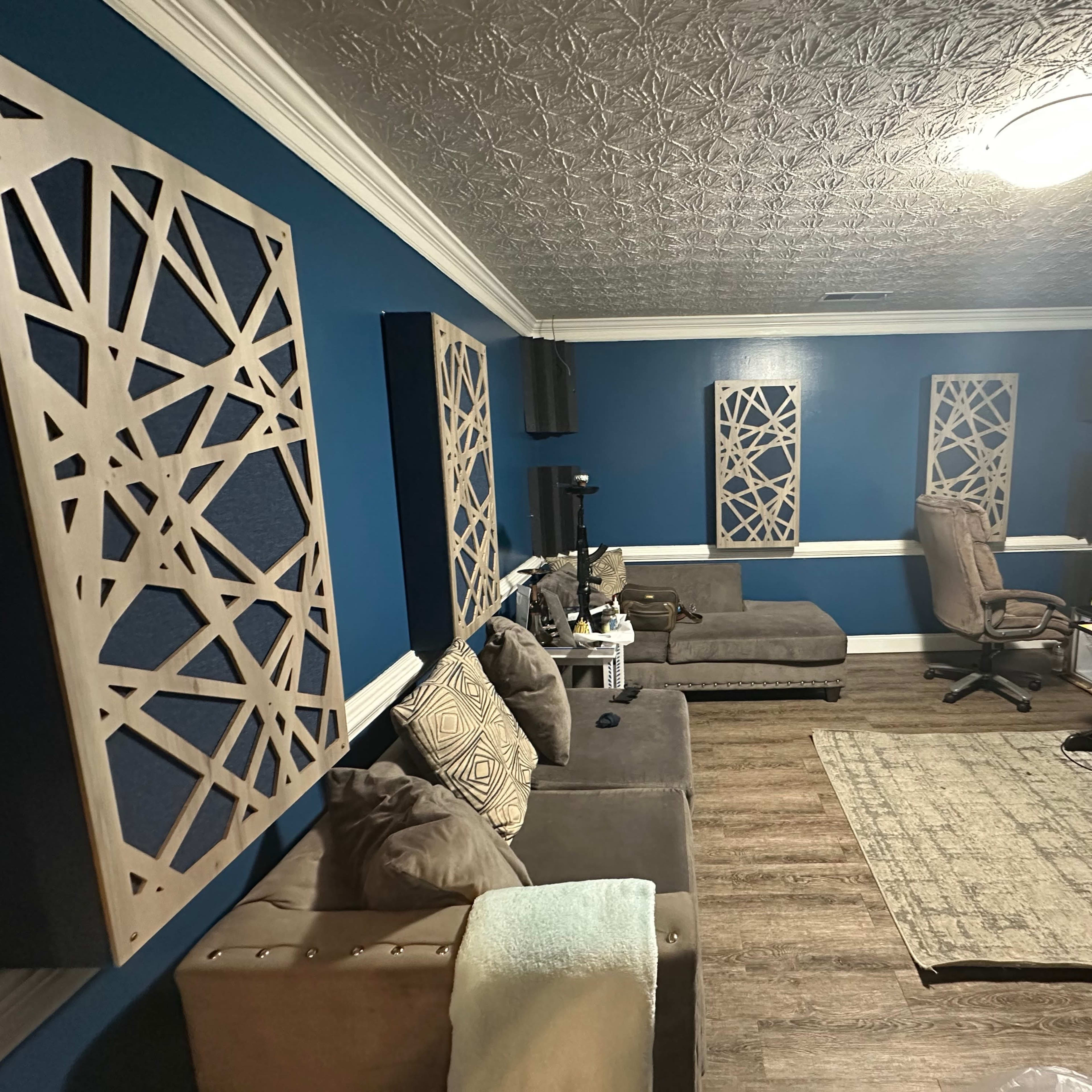 A room with blue walls, decorative wooden panels, a large rug, a seating area with two couches, and a workspace featuring a computer desk and monitors.