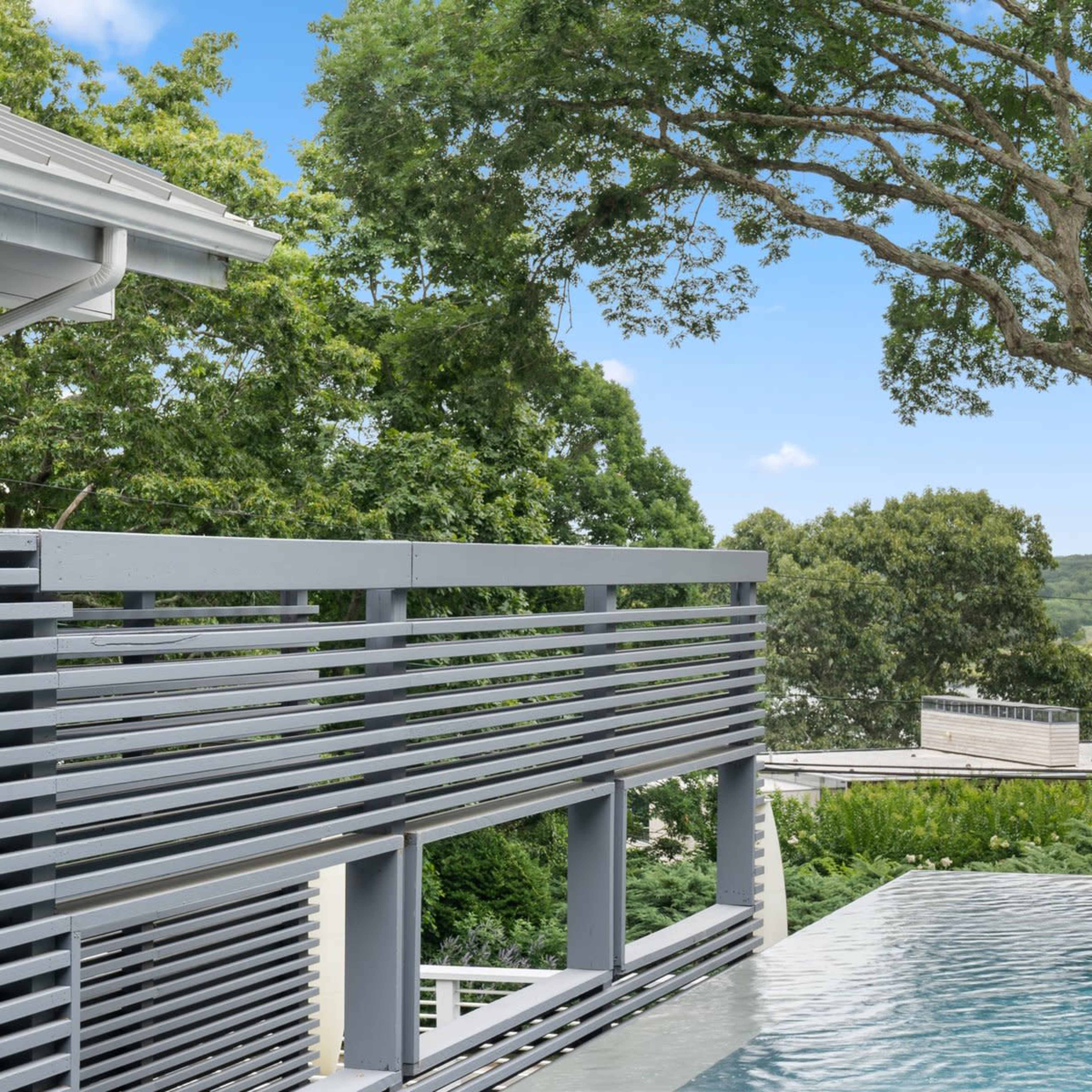 A modern pool with a reflective surface overlooks lush greenery and trees under a clear blue sky.