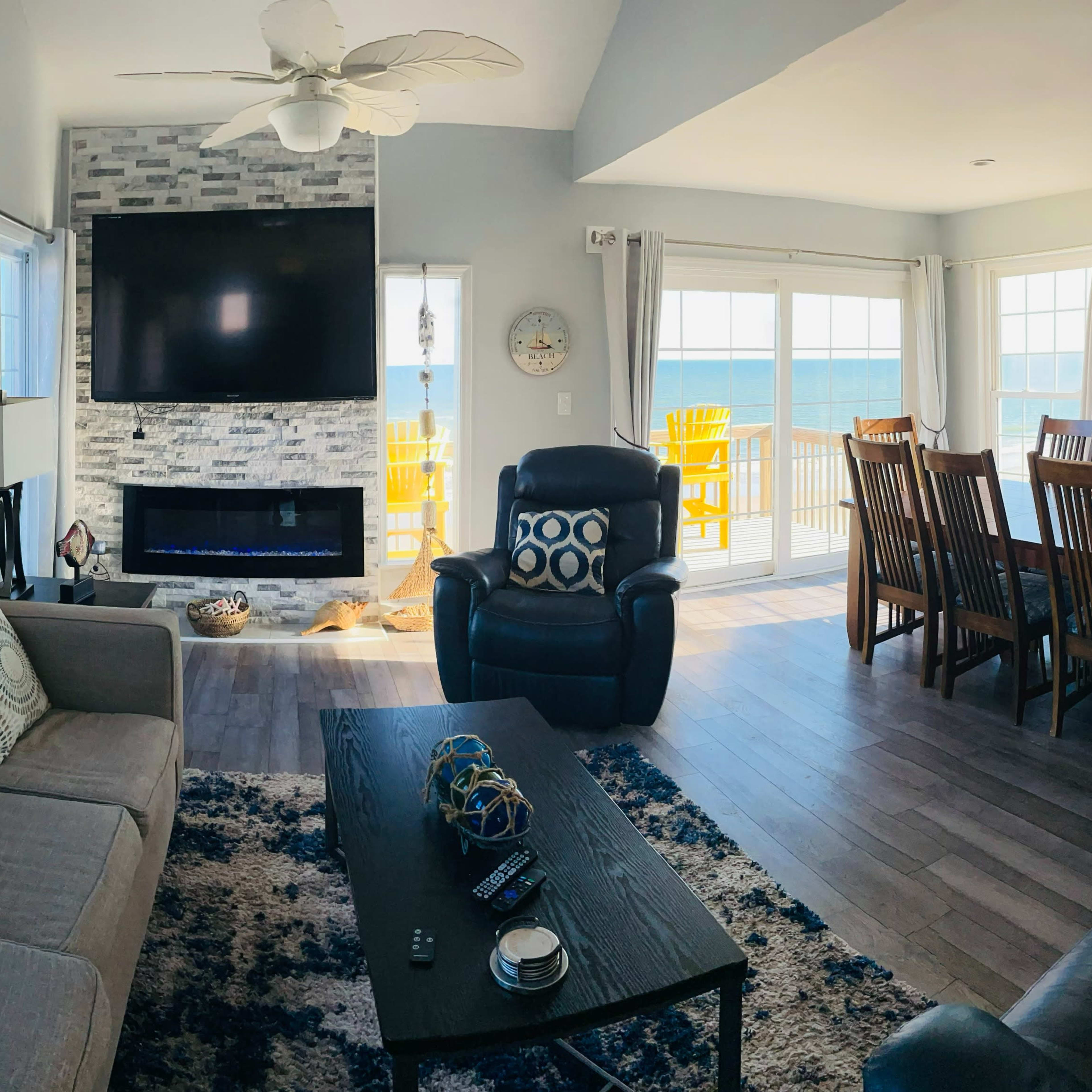 A coastal living room with a sectional sofa, a modern fireplace, and large windows revealing a view of the beach and ocean.