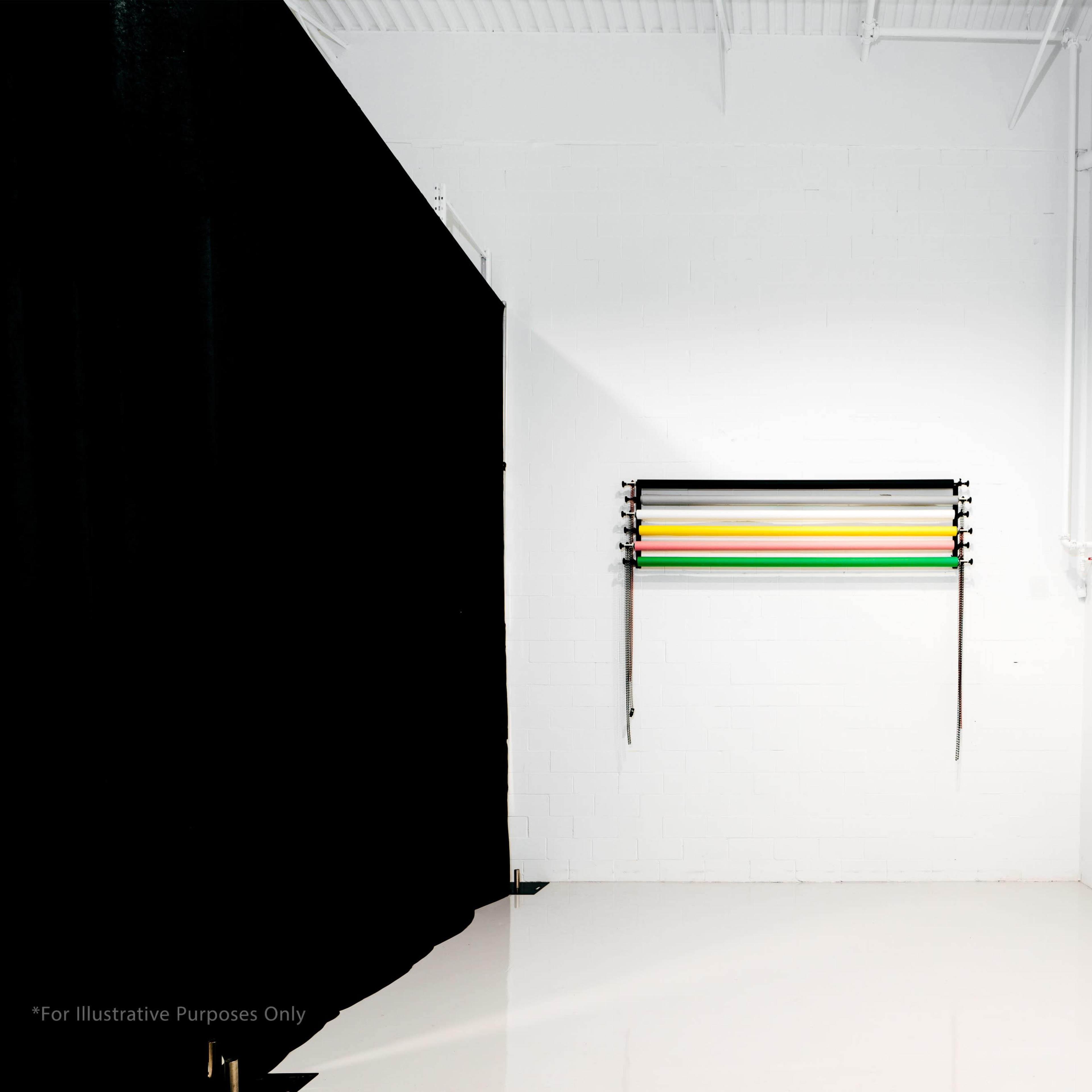 A minimalist studio space with a black curtain on the left and a row of colorful fabric strips suspended from a rack on the white wall.