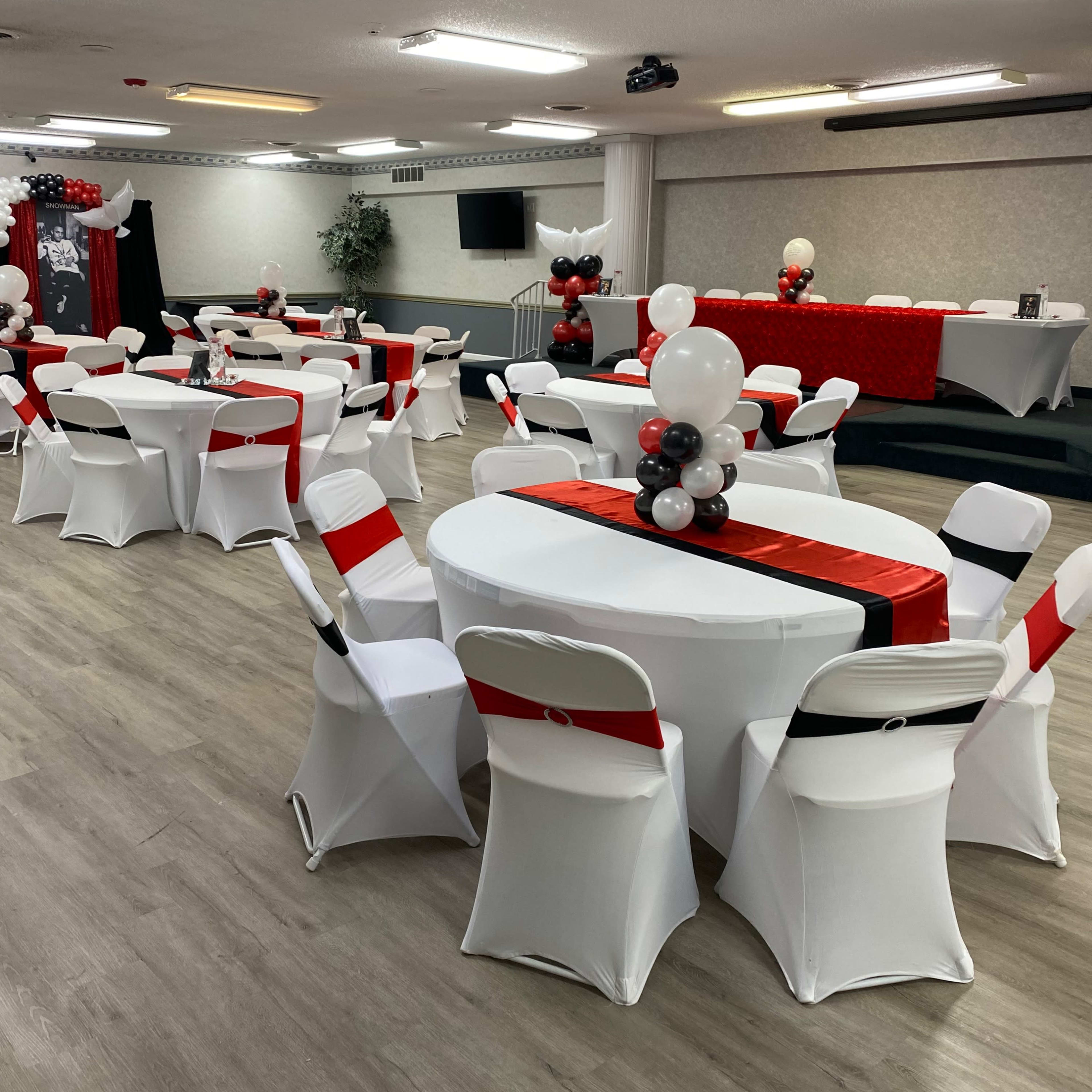 A decorated event space featuring white tables with red accents, white chairs, and balloon arrangements in black and white.