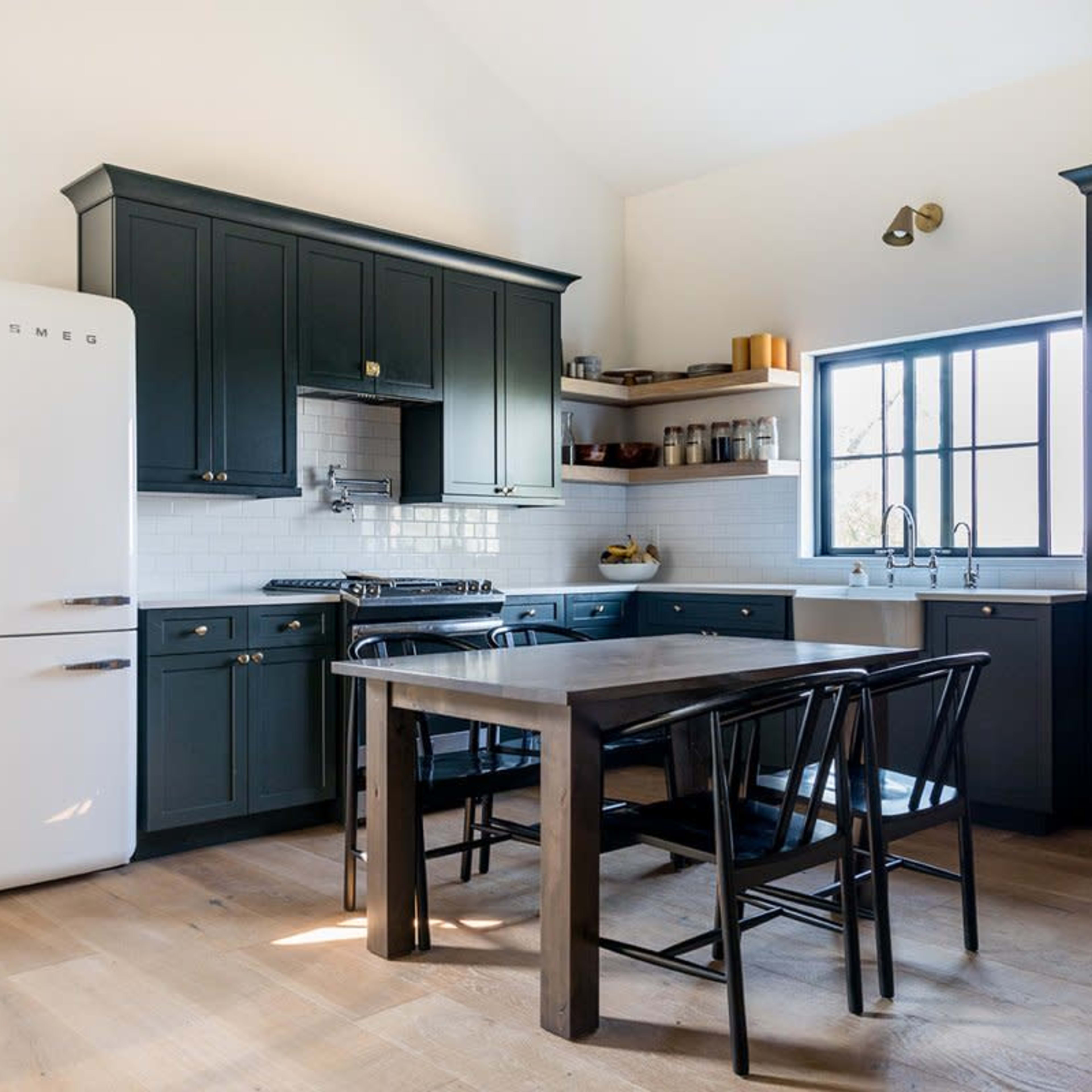 A modern kitchen with dark cabinets, a white refrigerator, a wooden dining table, and black chairs.