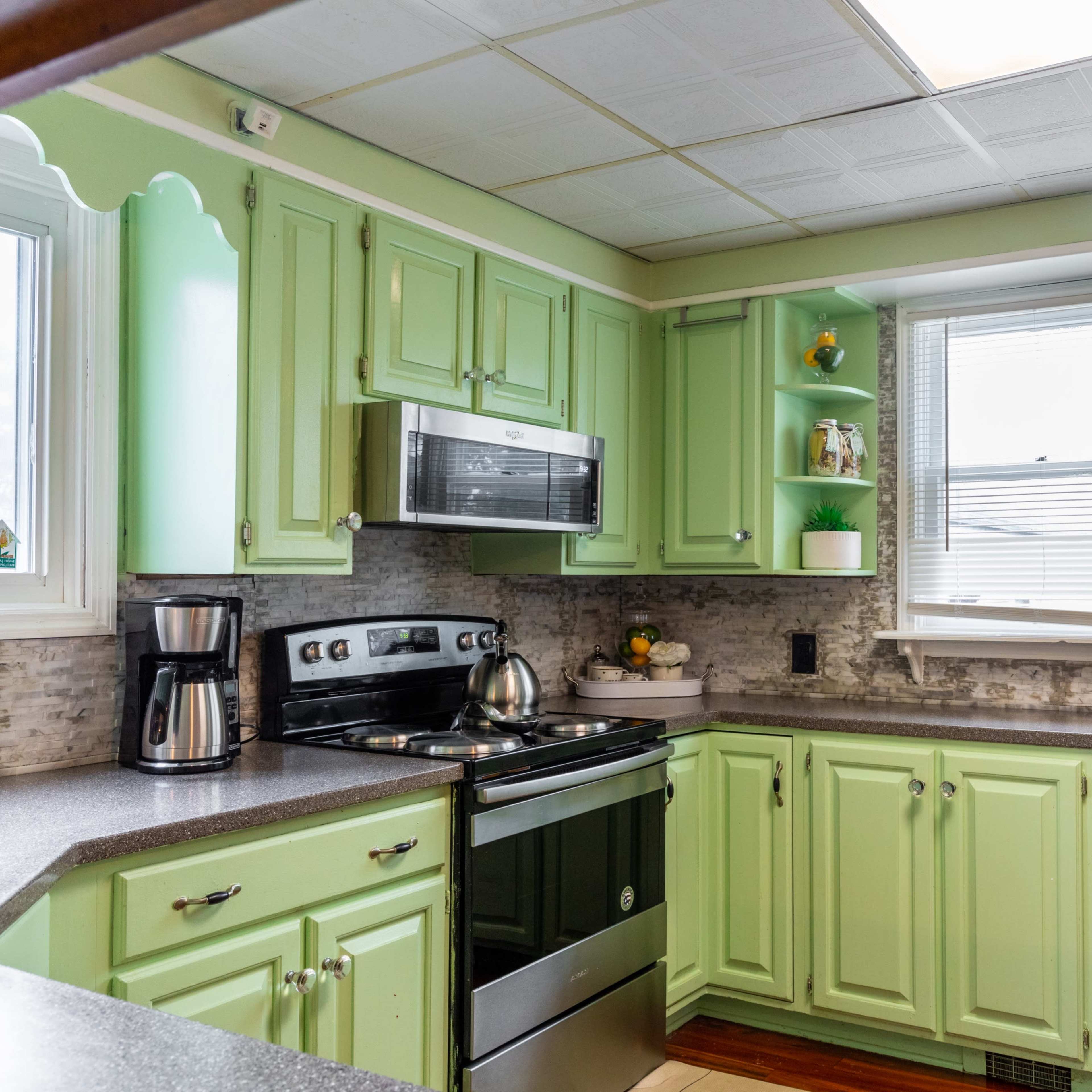 A kitchen with green cabinets, stainless steel appliances, and a window allowing natural light.