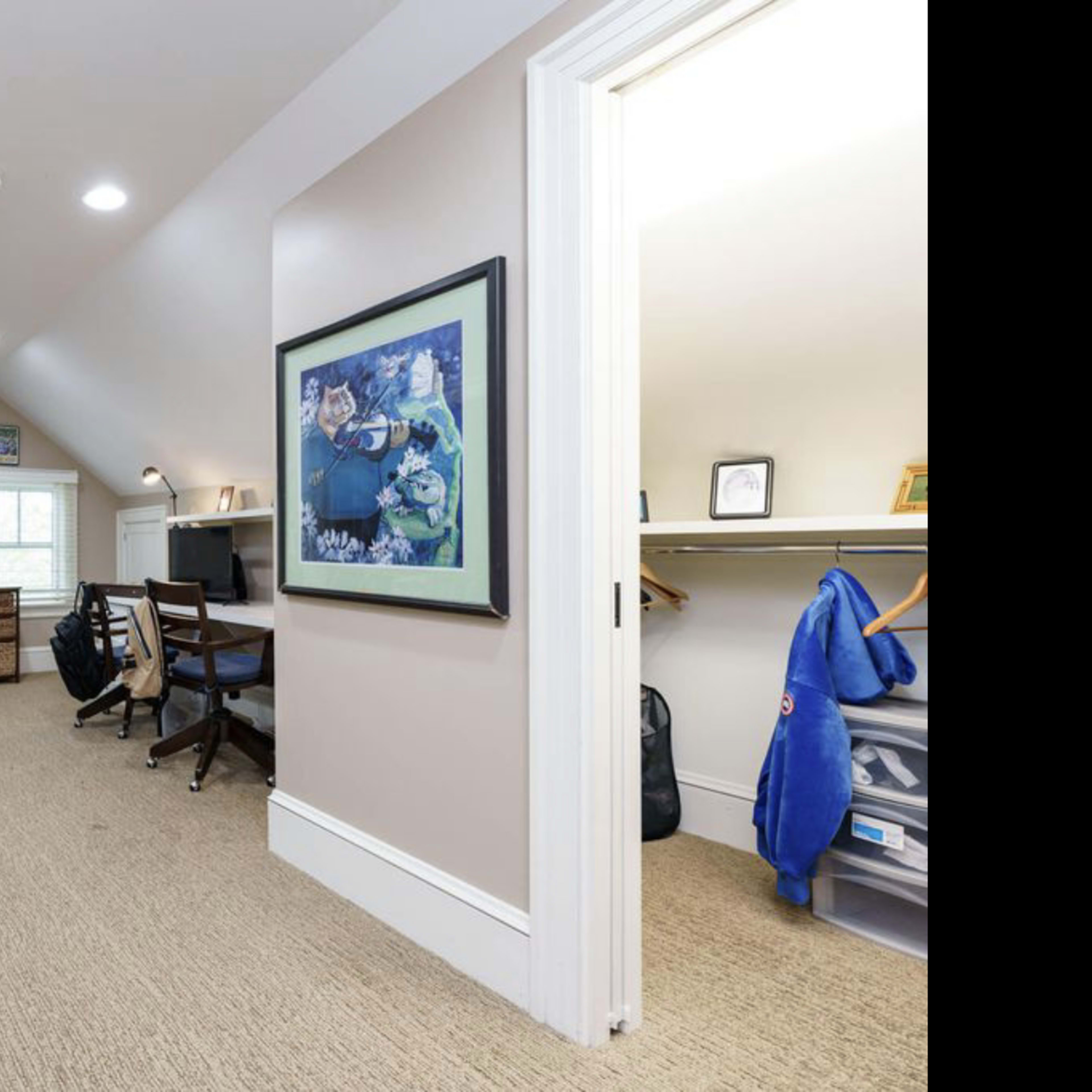 A well-lit, organized room with a desk, shelves, and bean bag chairs, featuring a large artwork on one wall.