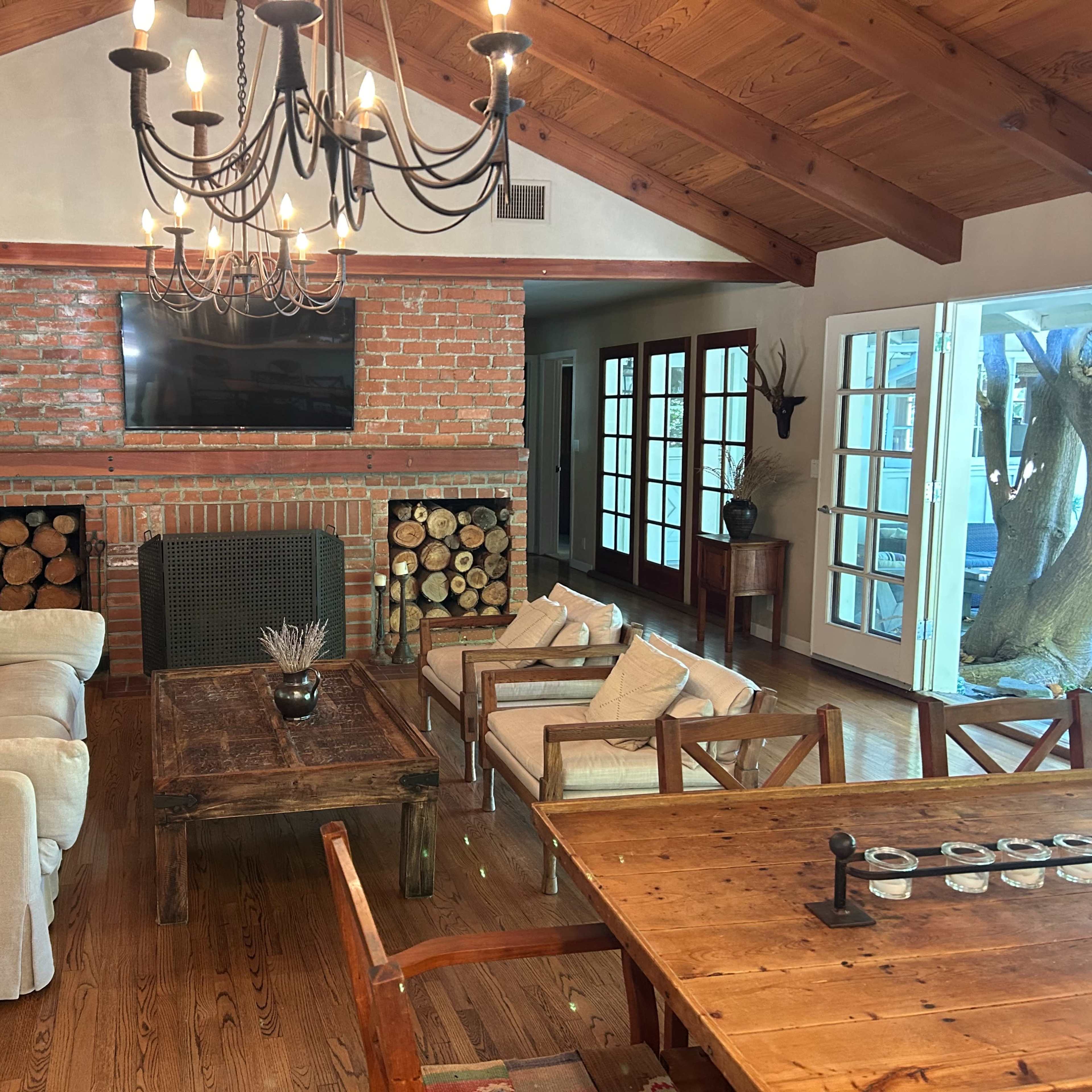 A cozy living room with a brick fireplace, wooden ceiling beams, and a mix of comfortable seating arrangements.