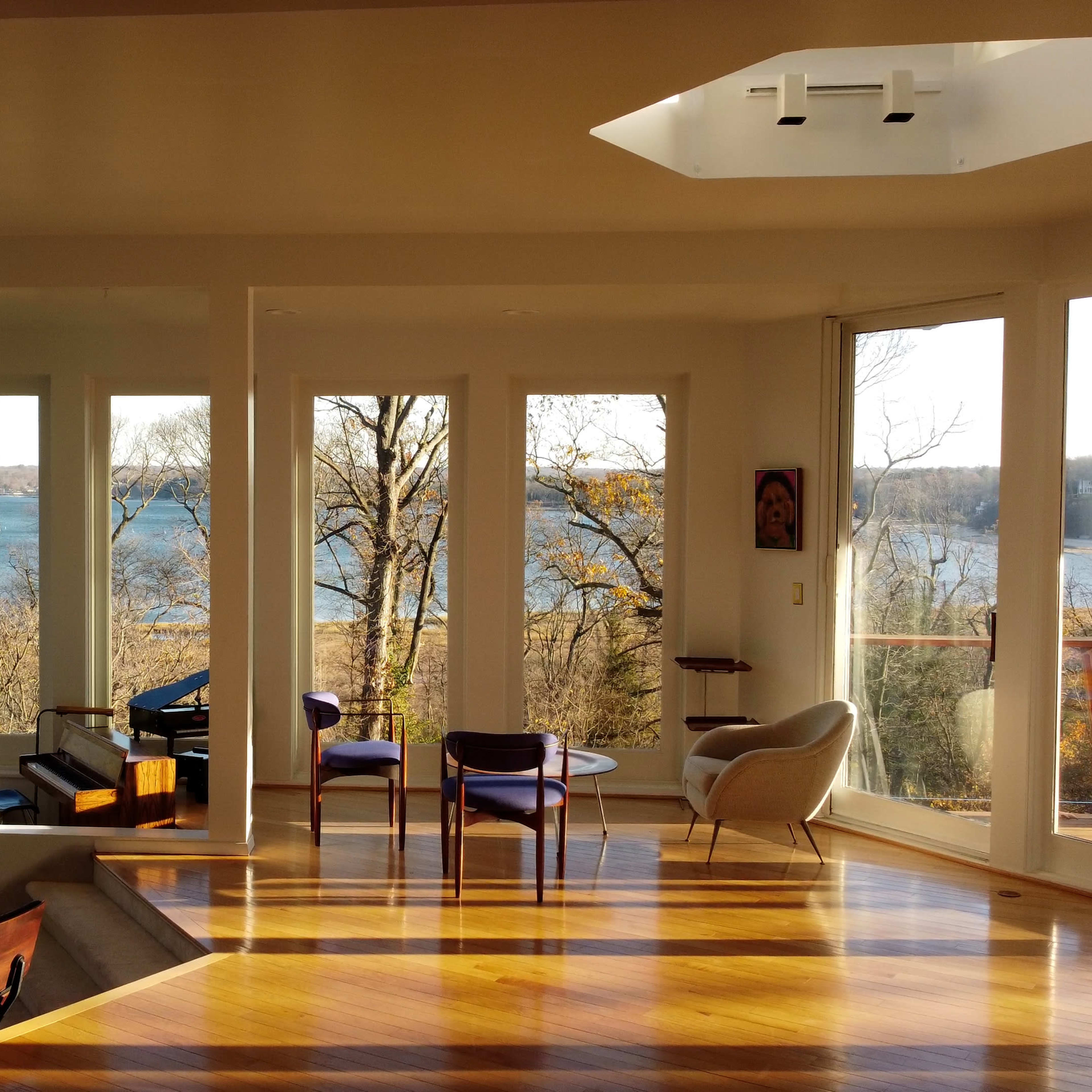 A spacious living area with large windows overlooking a body of water and trees in the distance.