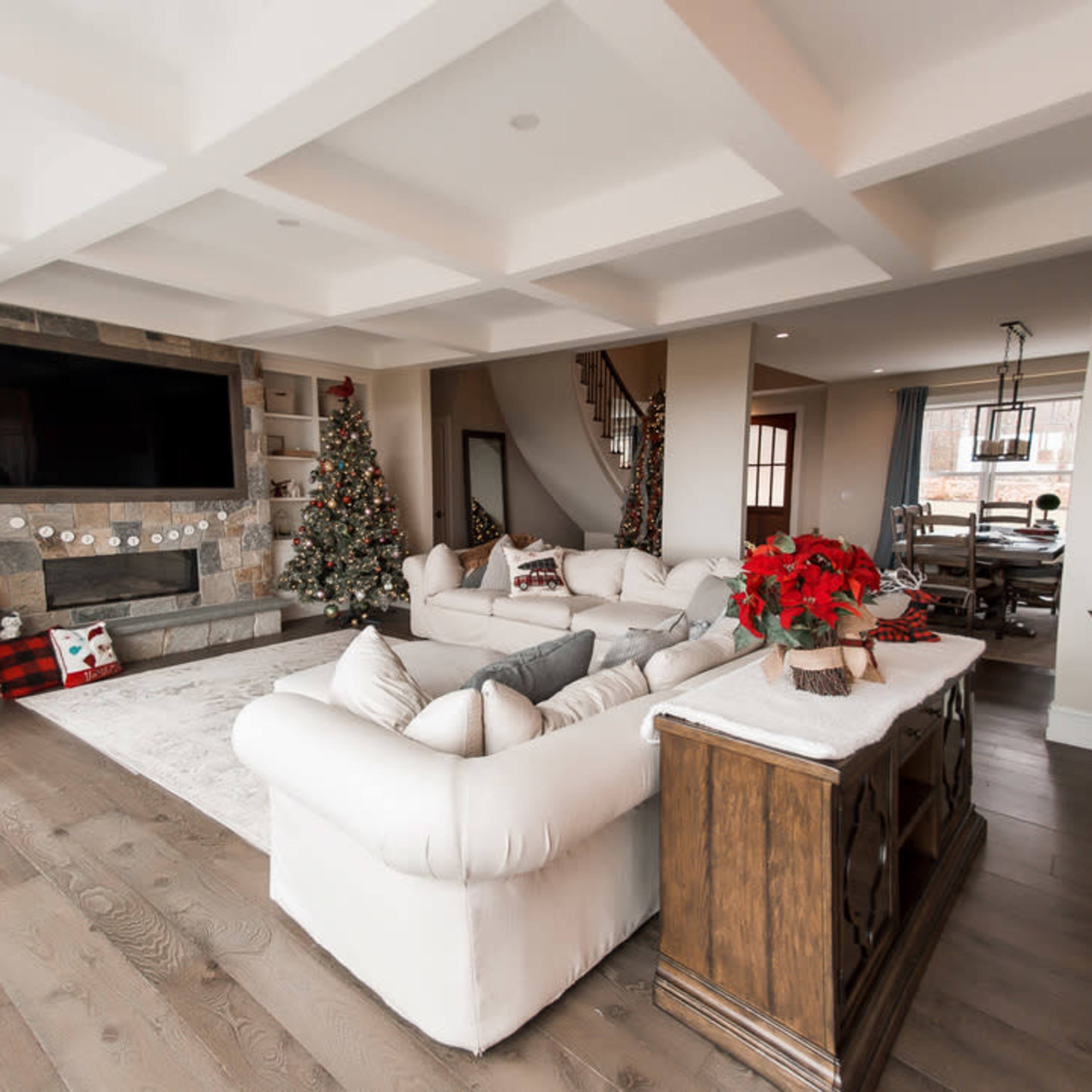 A spacious living room adorned with two Christmas trees, a large television mounted on the wall, and a decorative wooden cabinet.