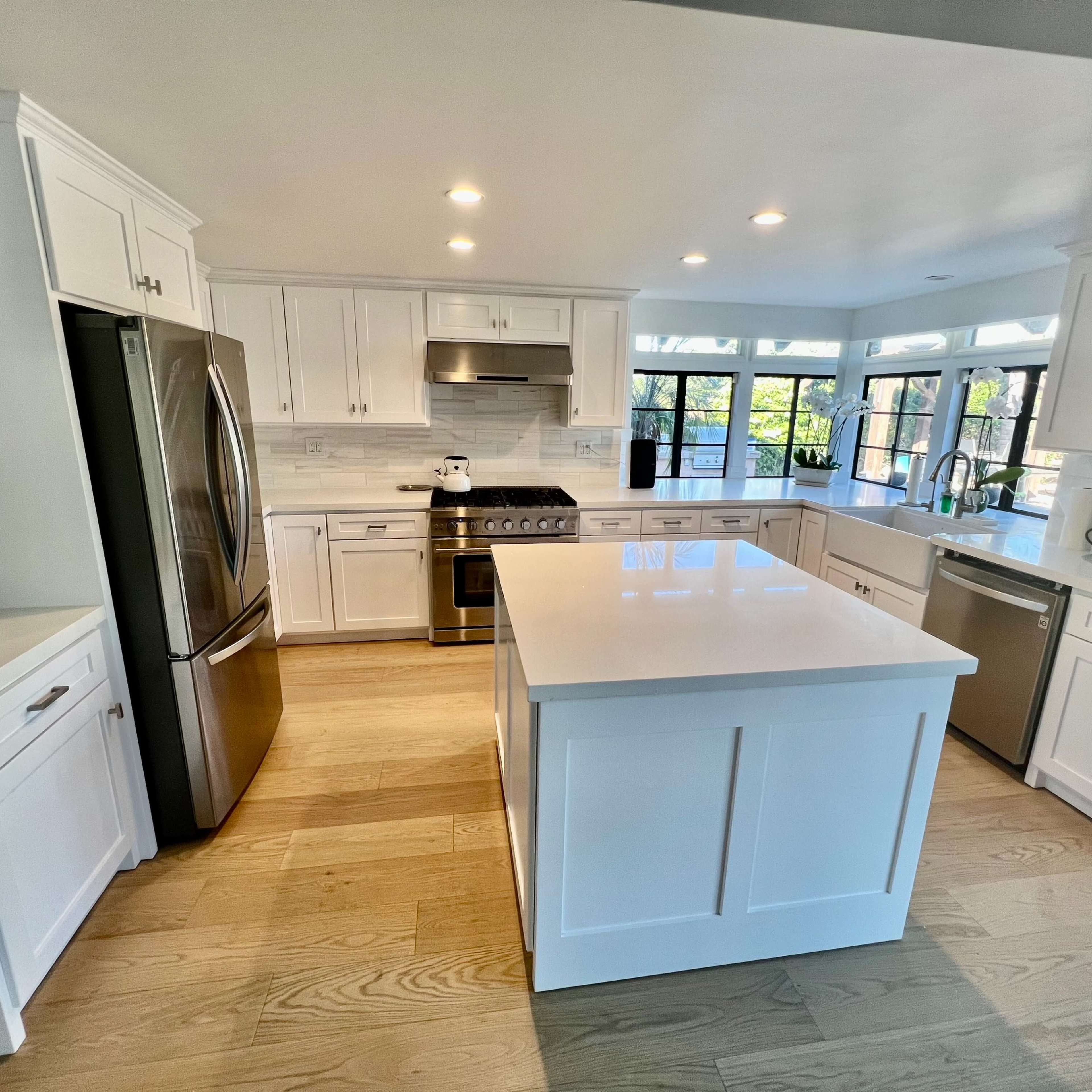 A modern kitchen features white cabinetry, stainless steel appliances, and a large central island with a light countertop.