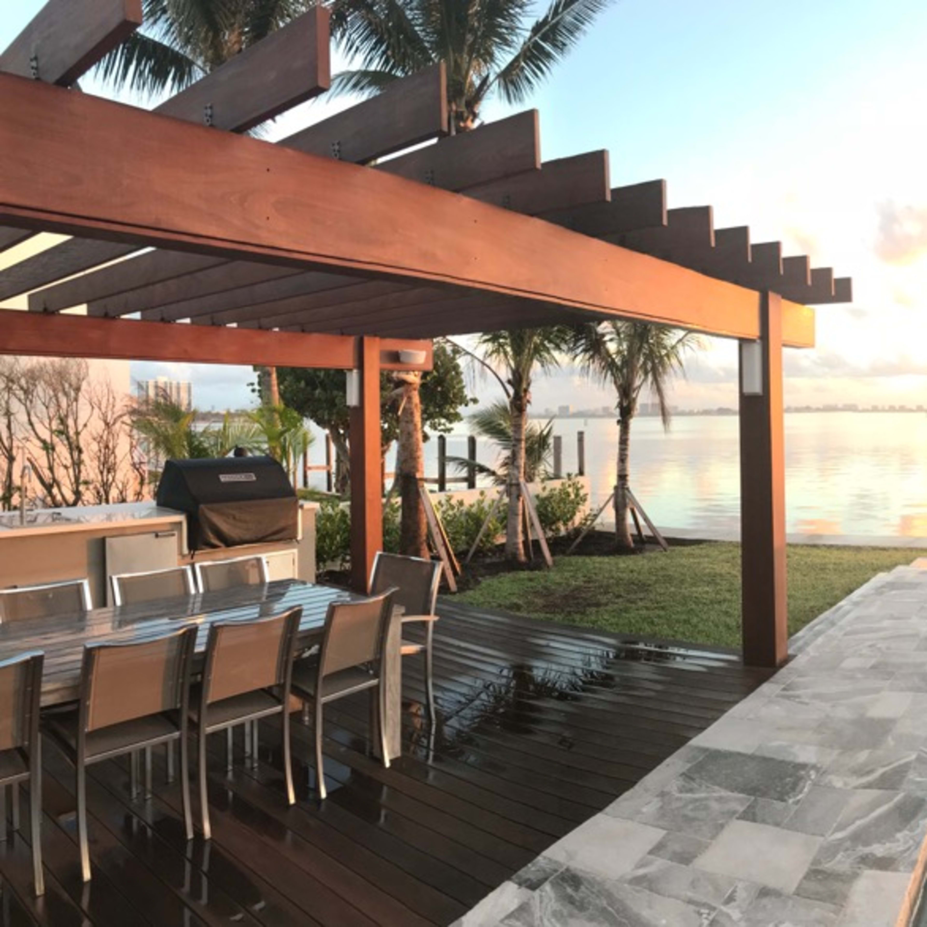 A waterfront property with a swimming pool, outdoor dining area, and a clear view of a sunrise over the water.