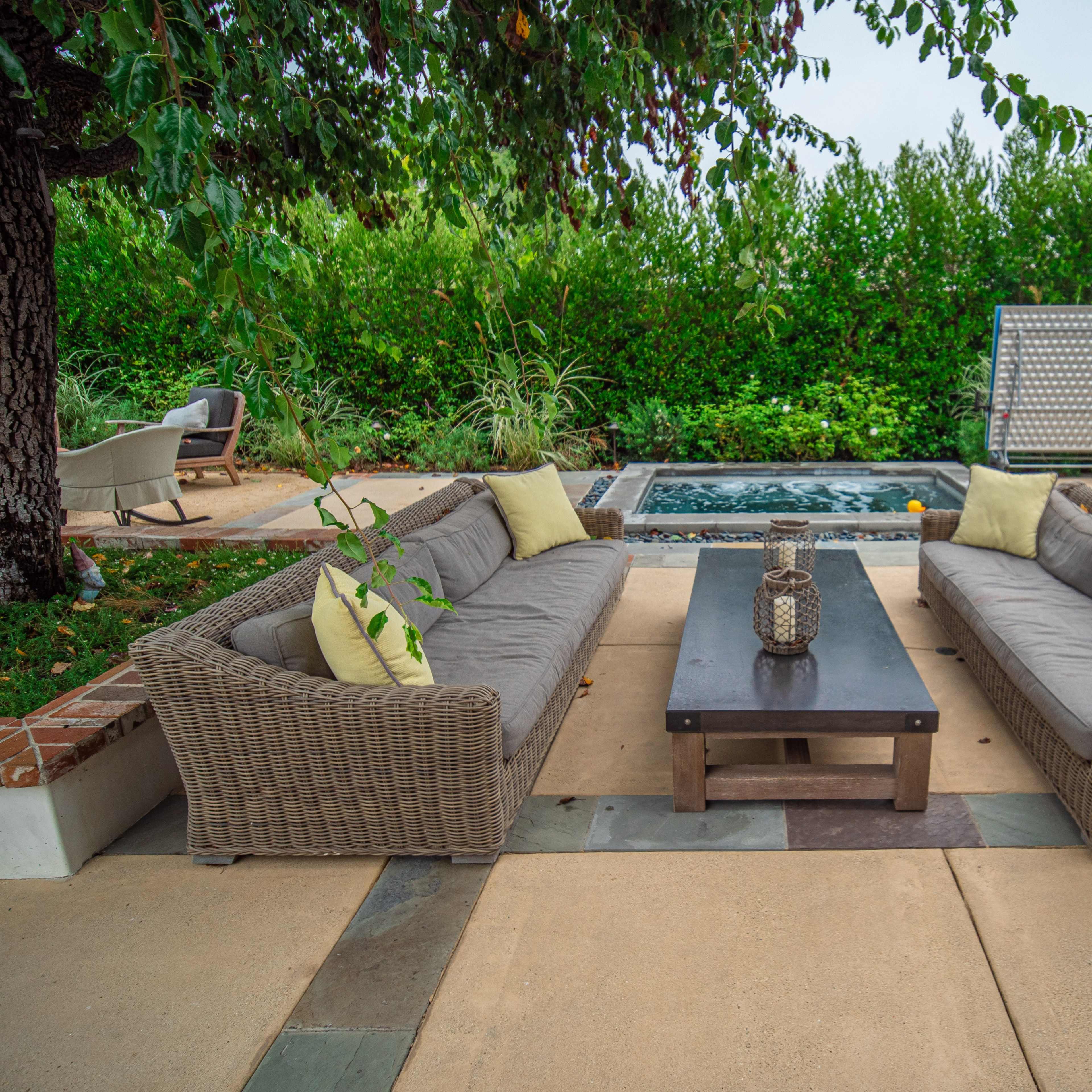 A patio area with two sectional sofas facing each other around a coffee table, surrounded by greenery and a small water feature.