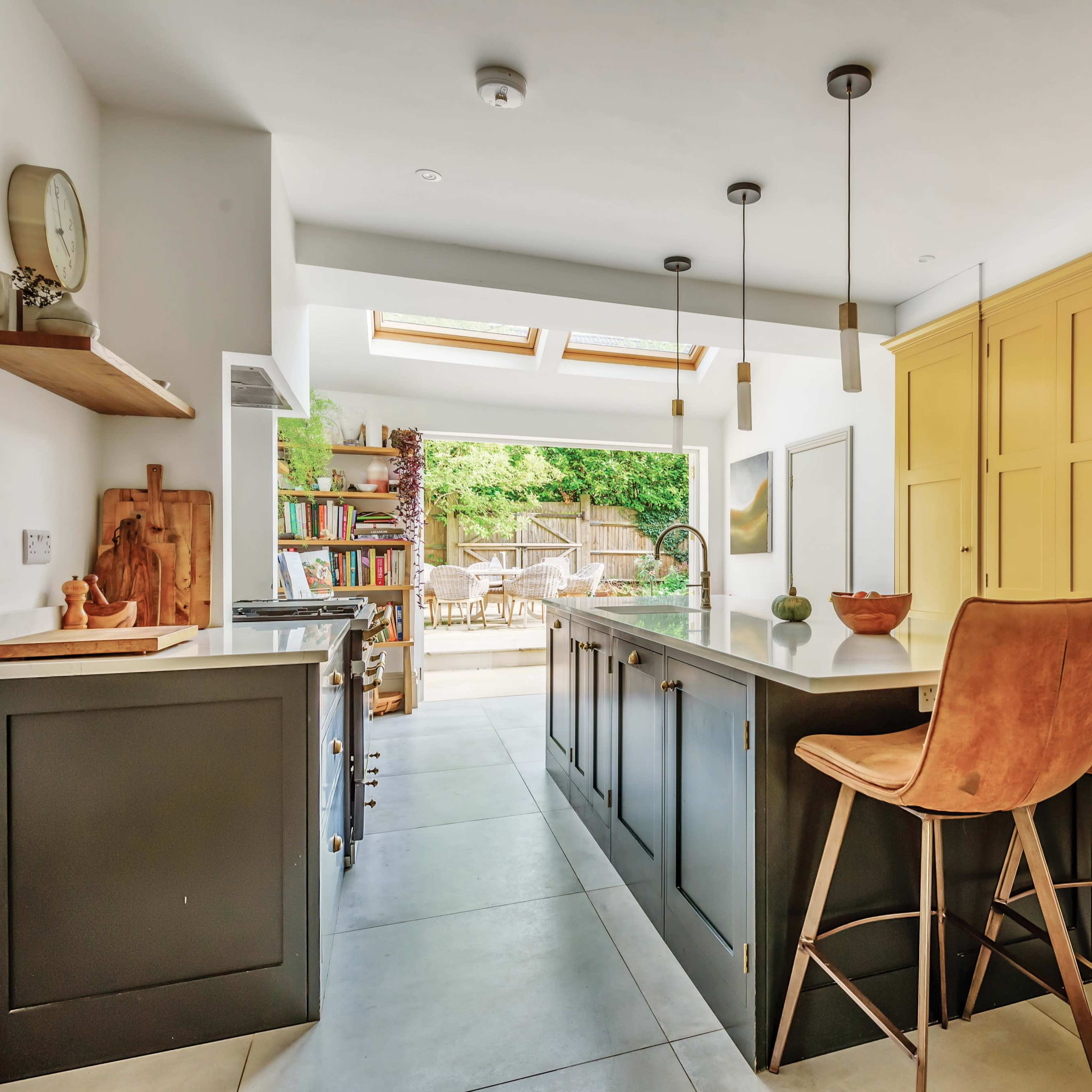 The kitchen features a central island with bar stools, yellow cabinetry, and large skylights providing natural light.