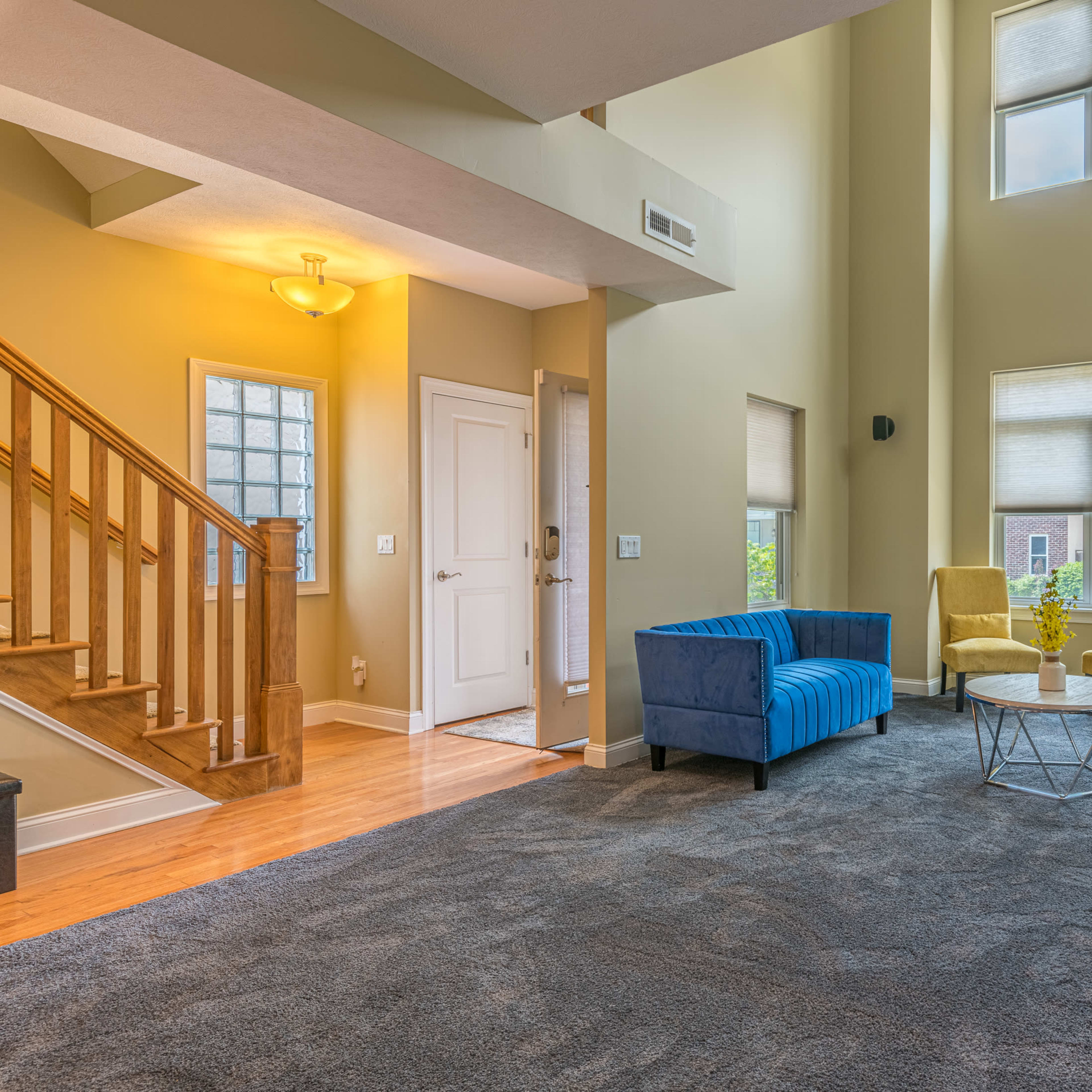 The living room features a blue sofa, a round coffee table, and tall windows that allow natural light to fill the space.
