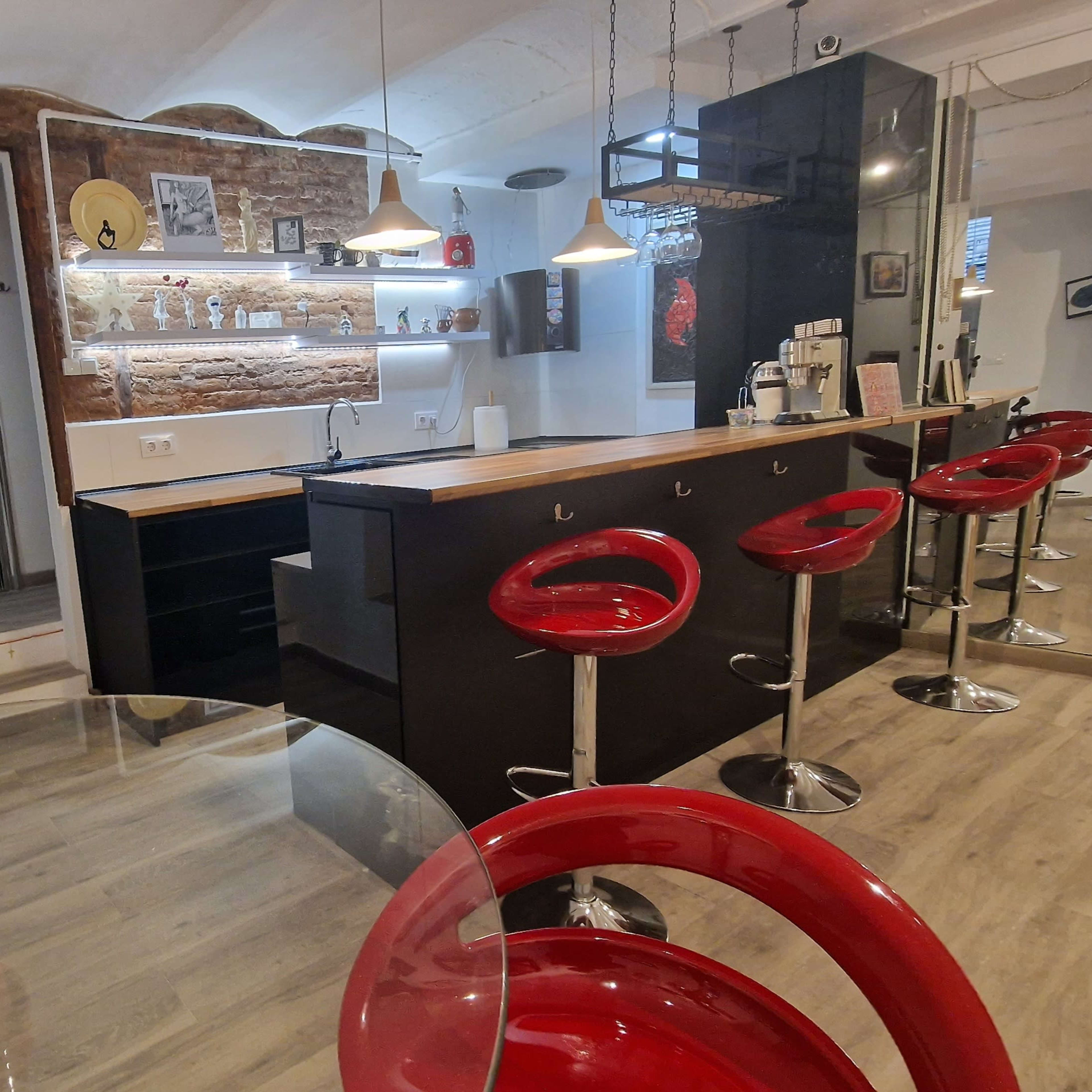 A modern kitchen and dining area featuring a bar counter with high red stools, a potted plant sculpture, and a brick accent wall.