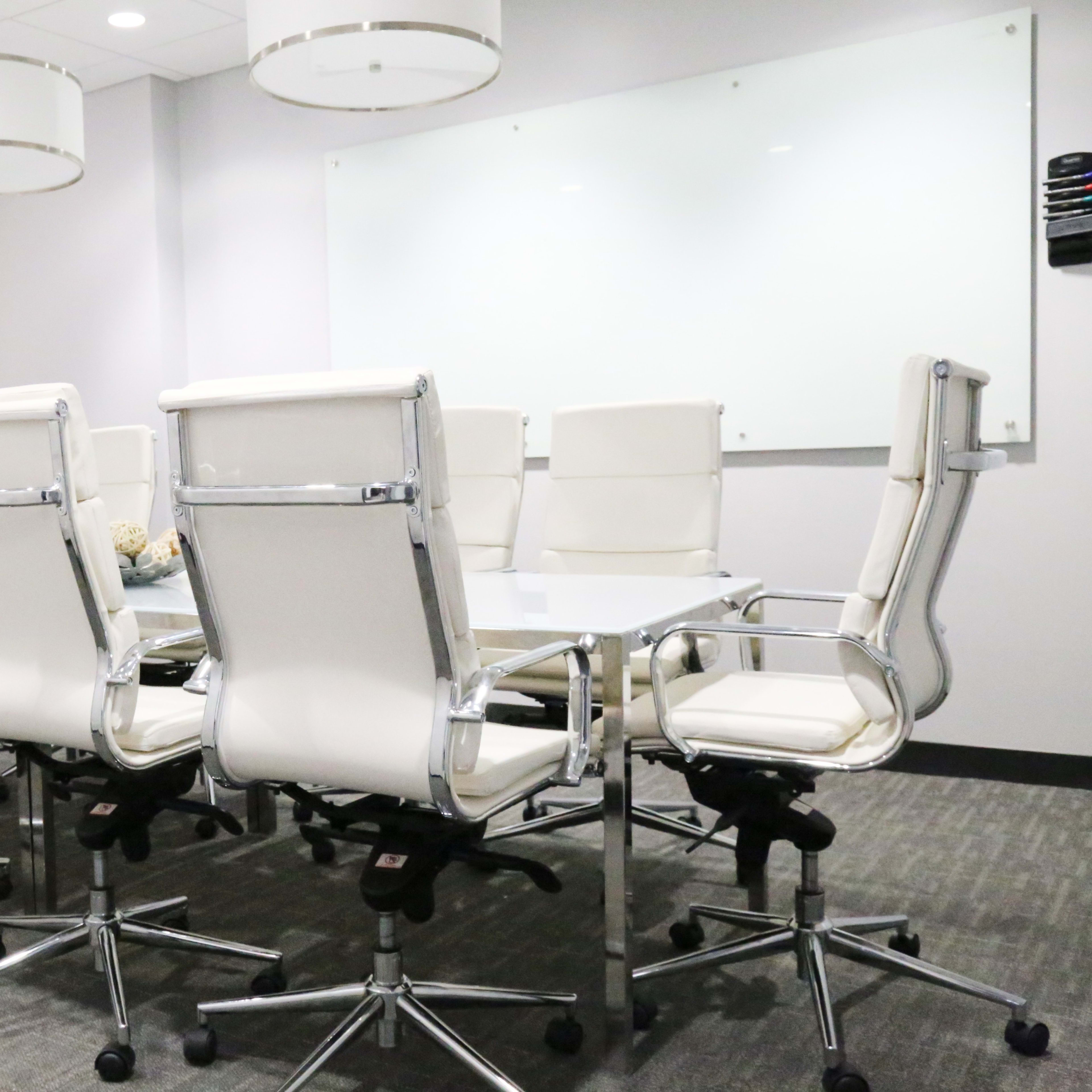 A modern conference room features a large table surrounded by white ergonomic chairs and minimalistic decor.