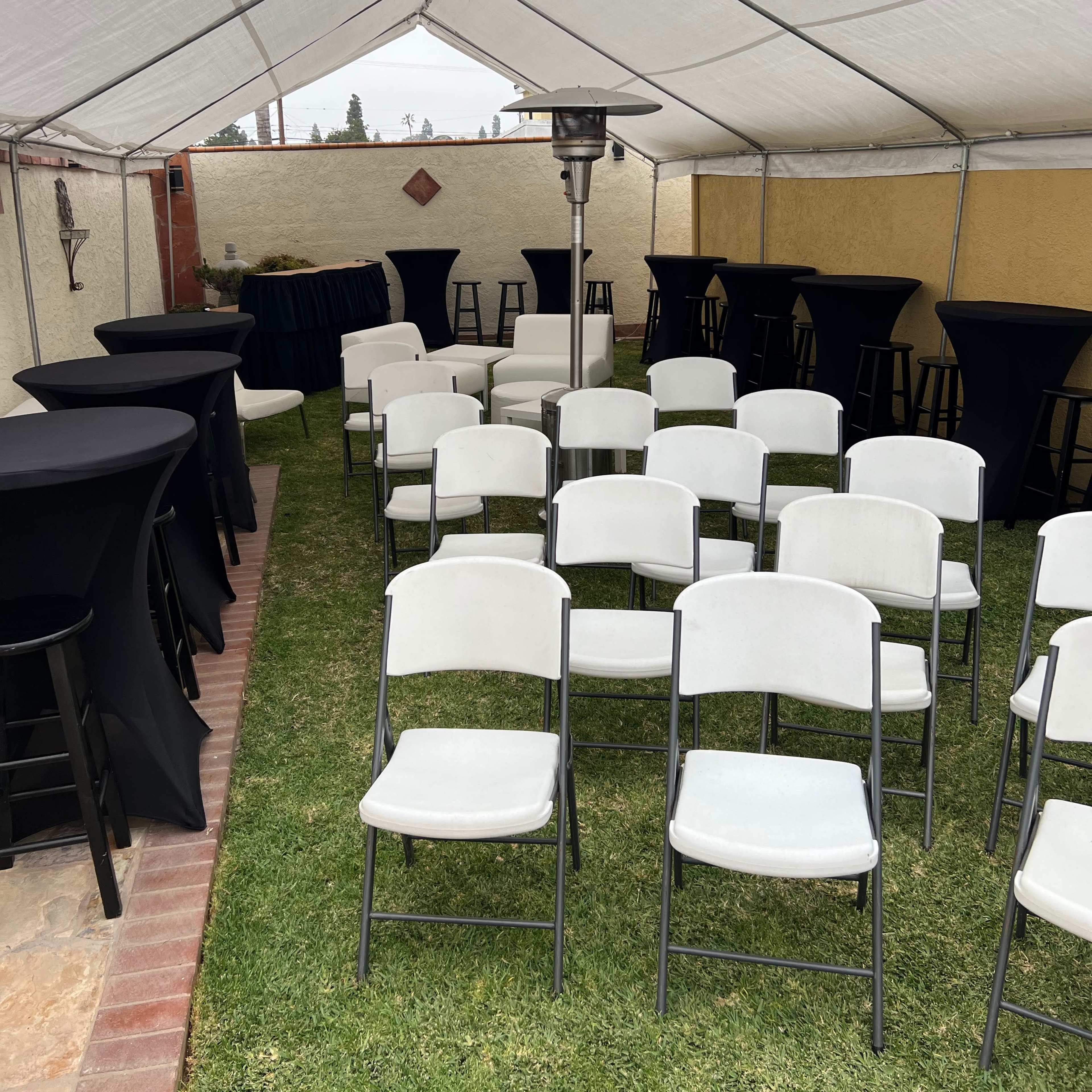 A tent set up with several rows of white folding chairs and black high-top tables on a grassy area.