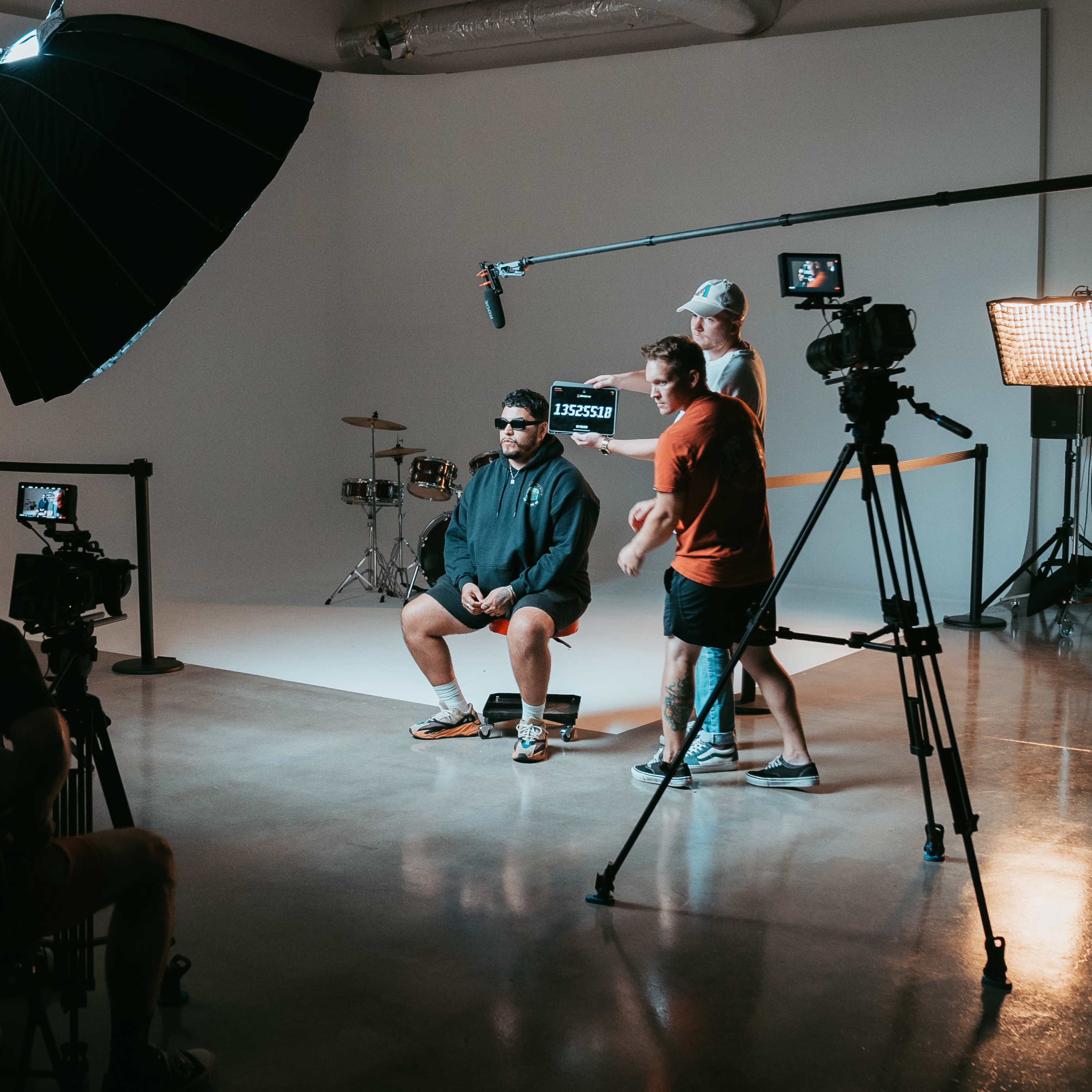 A small film crew sets up equipment around a seated subject in a photography studio.