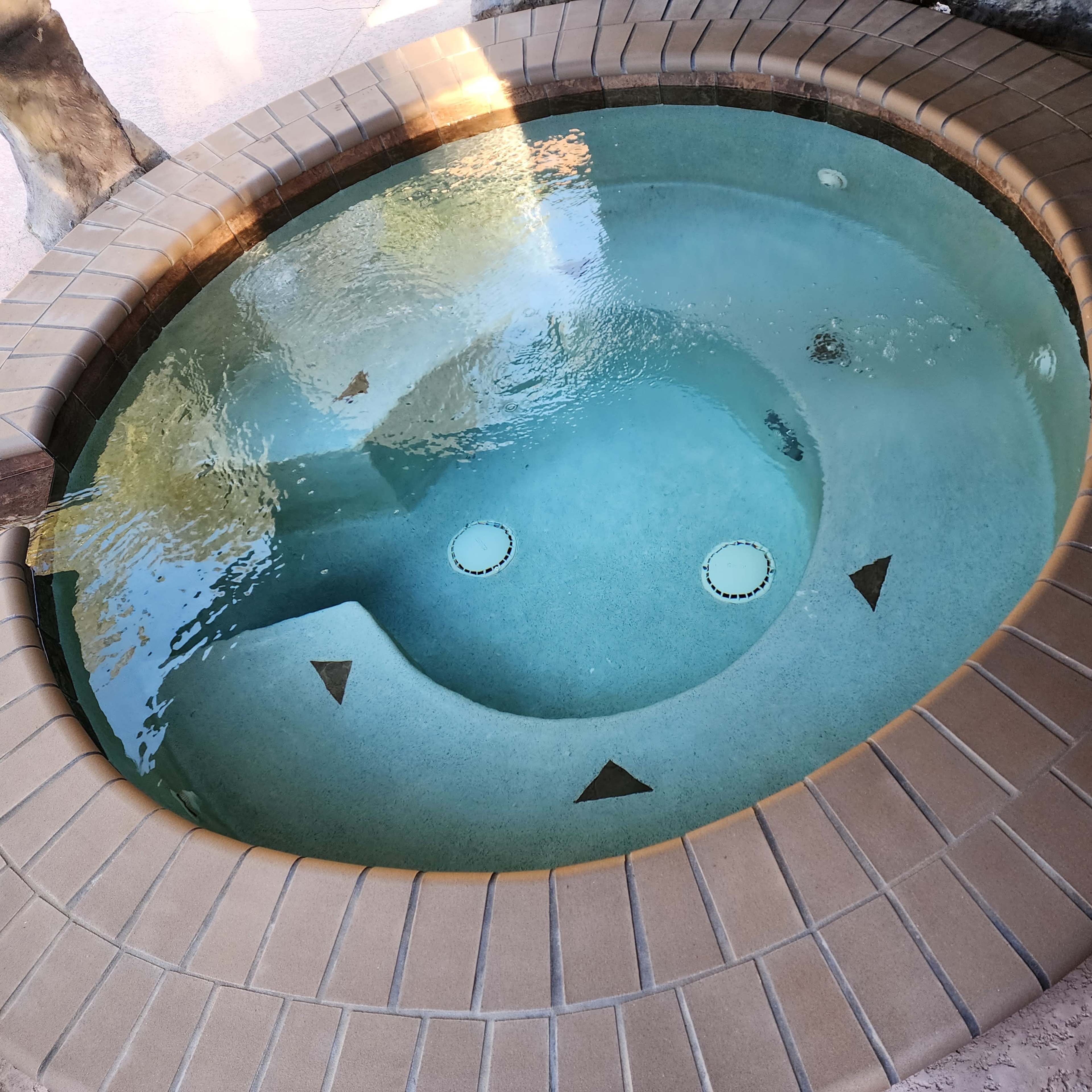 A circular hot tub with a tiled edge, featuring two circular jets and a smooth, clear water surface.