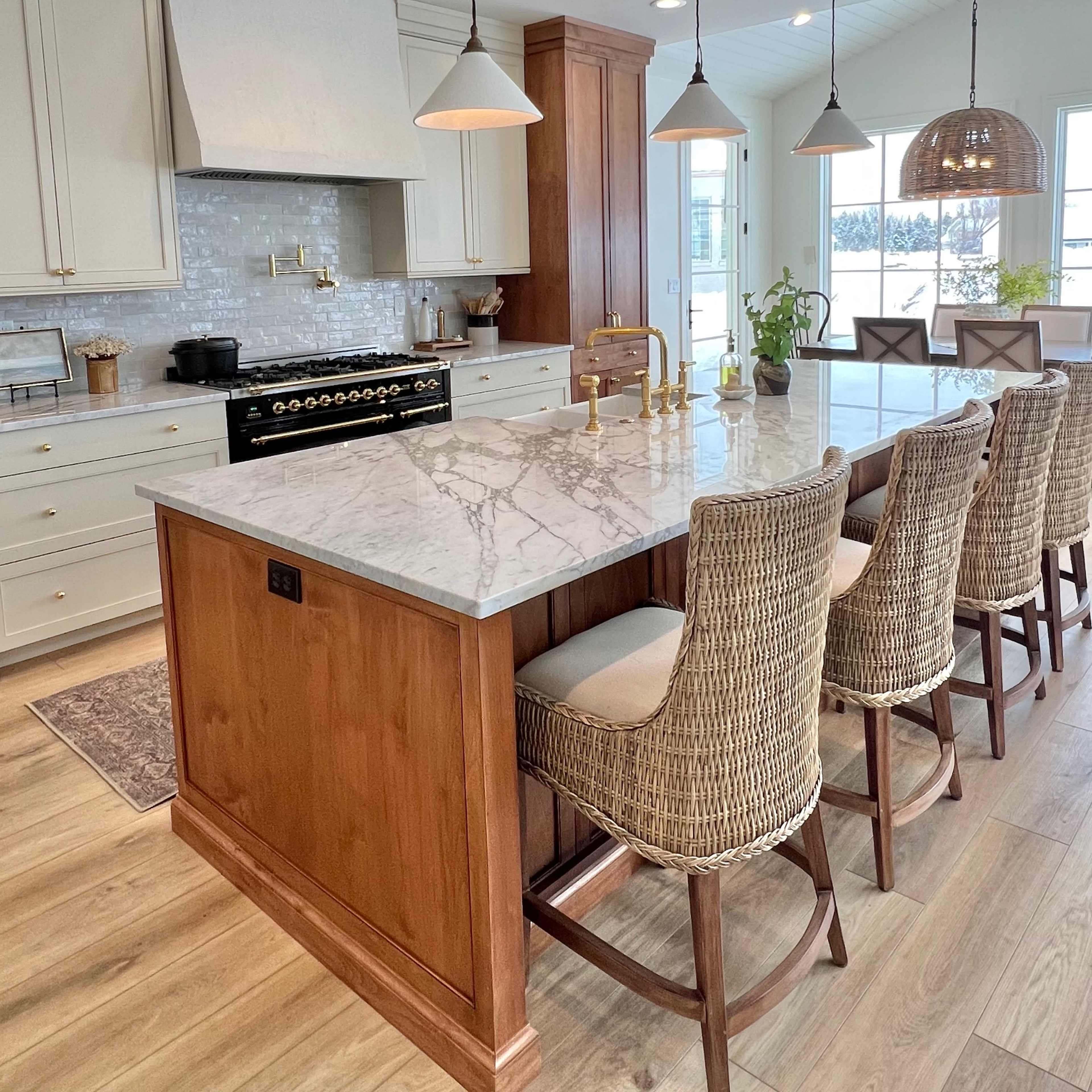 A modern kitchen with a large marble countertop, wooden cabinetry, and a row of woven bar stools.
