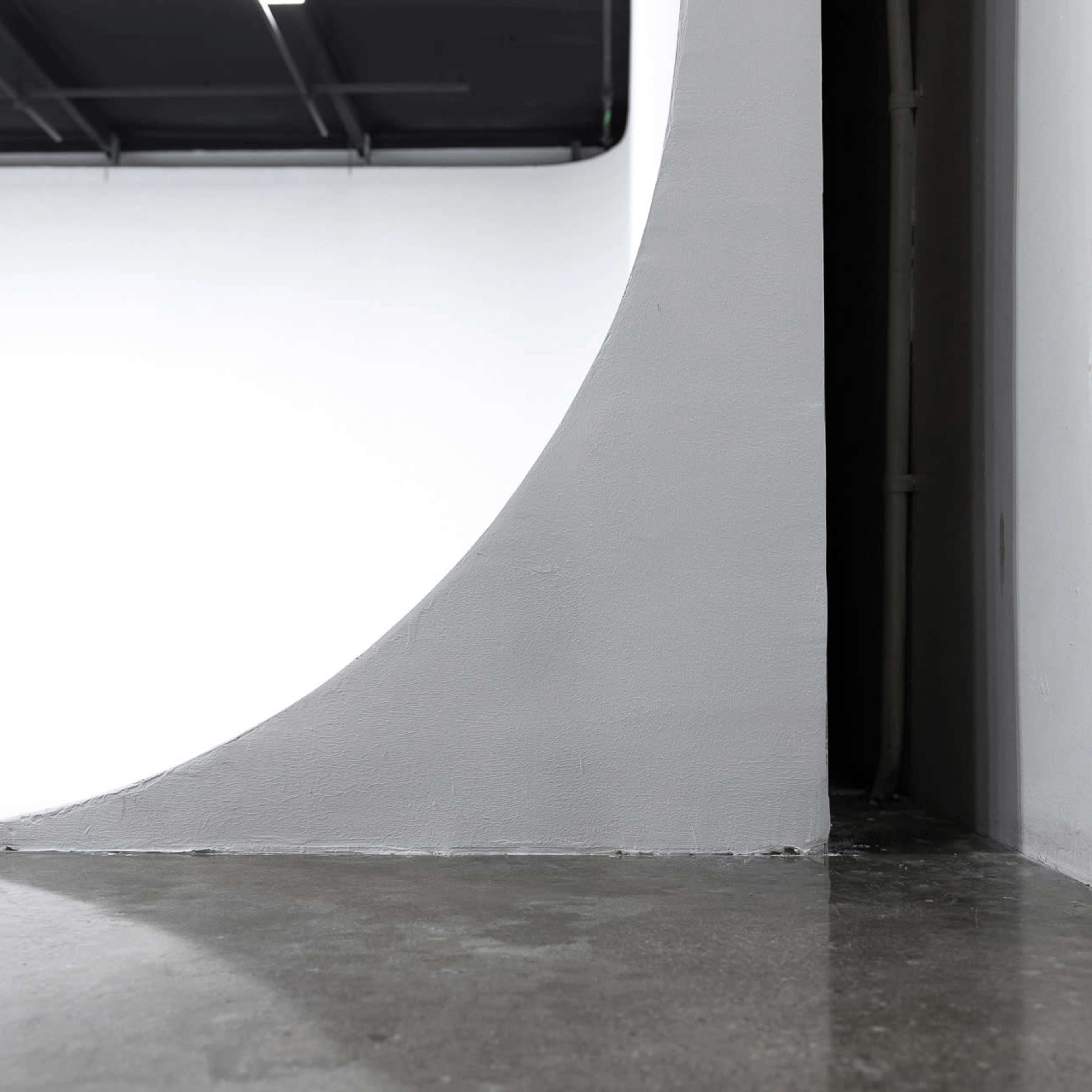 A minimalist interior space featuring a curved white wall meeting a concrete floor in an industrial setting.