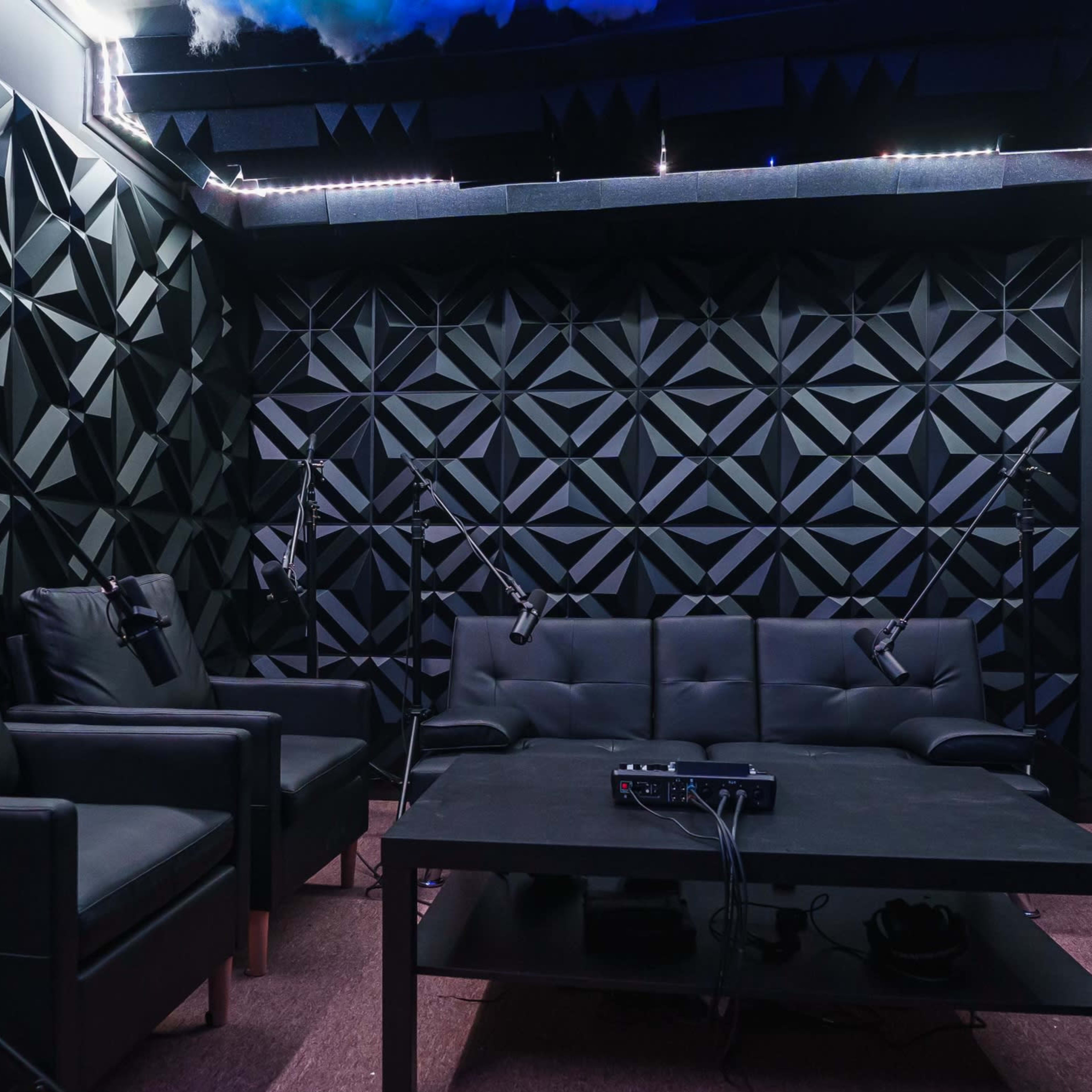 A soundproof recording studio with black geometric-patterned walls, a black sofa, and multiple microphones set up on stands.