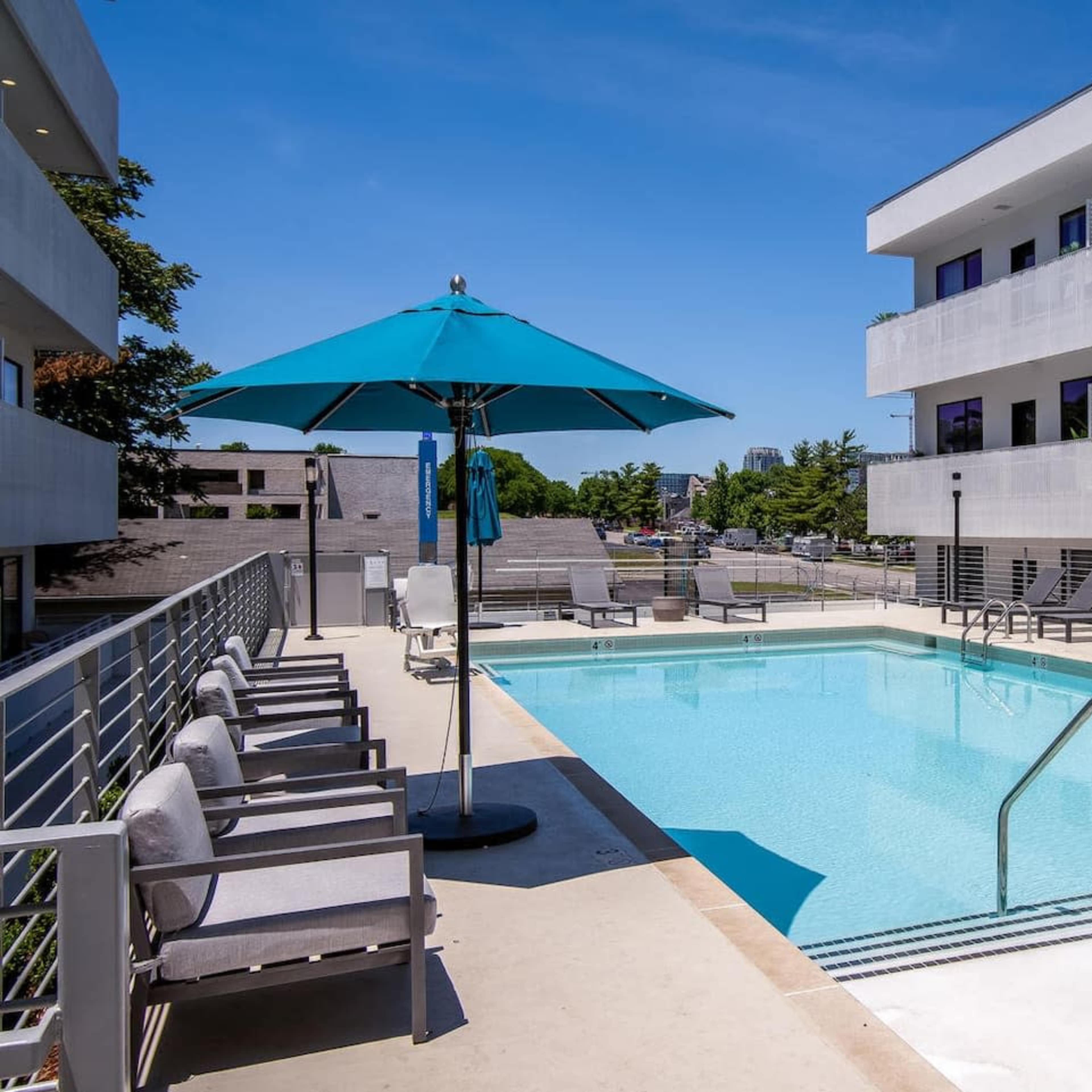 A modern outdoor pool area with lounge chairs, umbrellas, and a sleek building in the background.