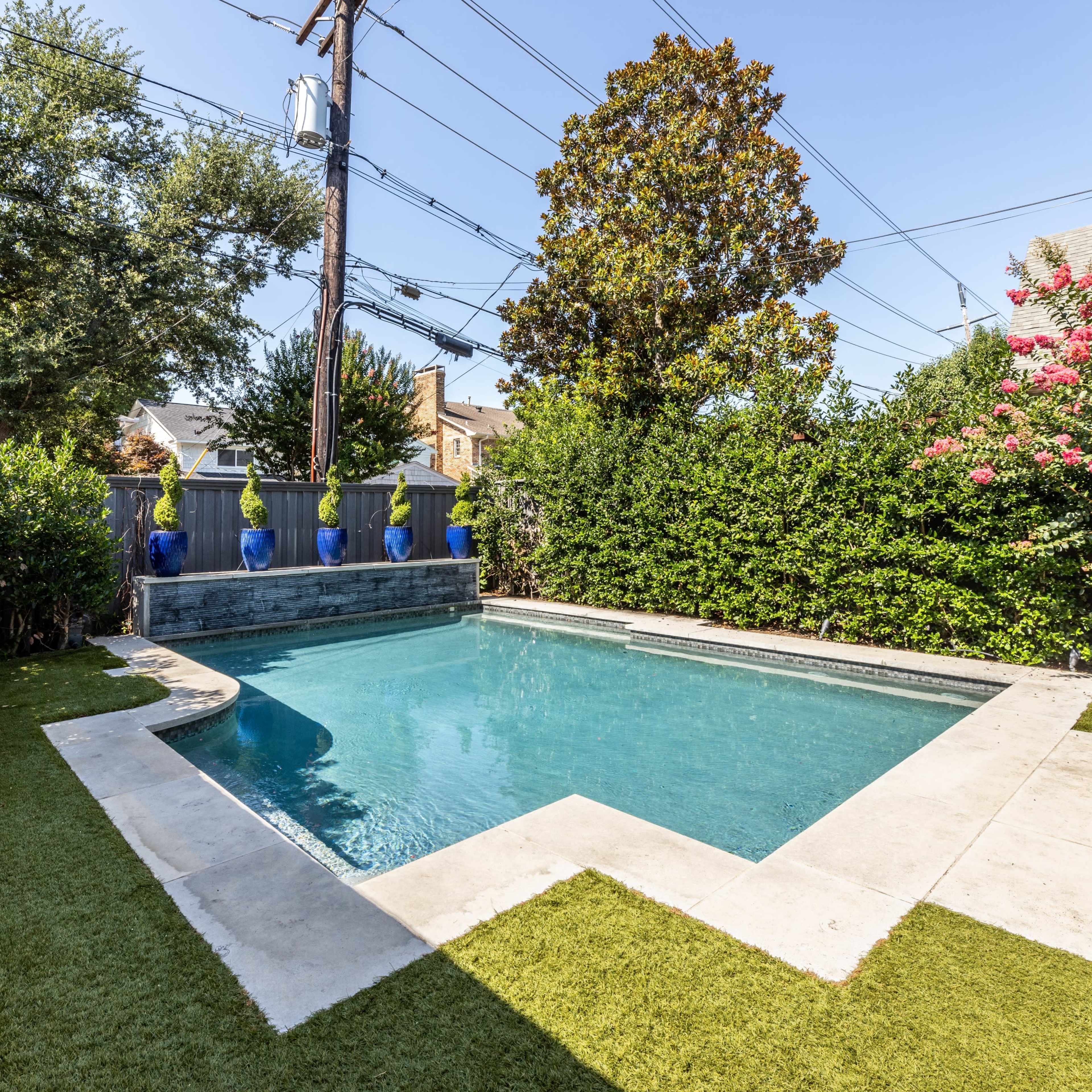 A rectangular swimming pool surrounded by green grass and hedges, with decorative blue pots placed near the perimeter.