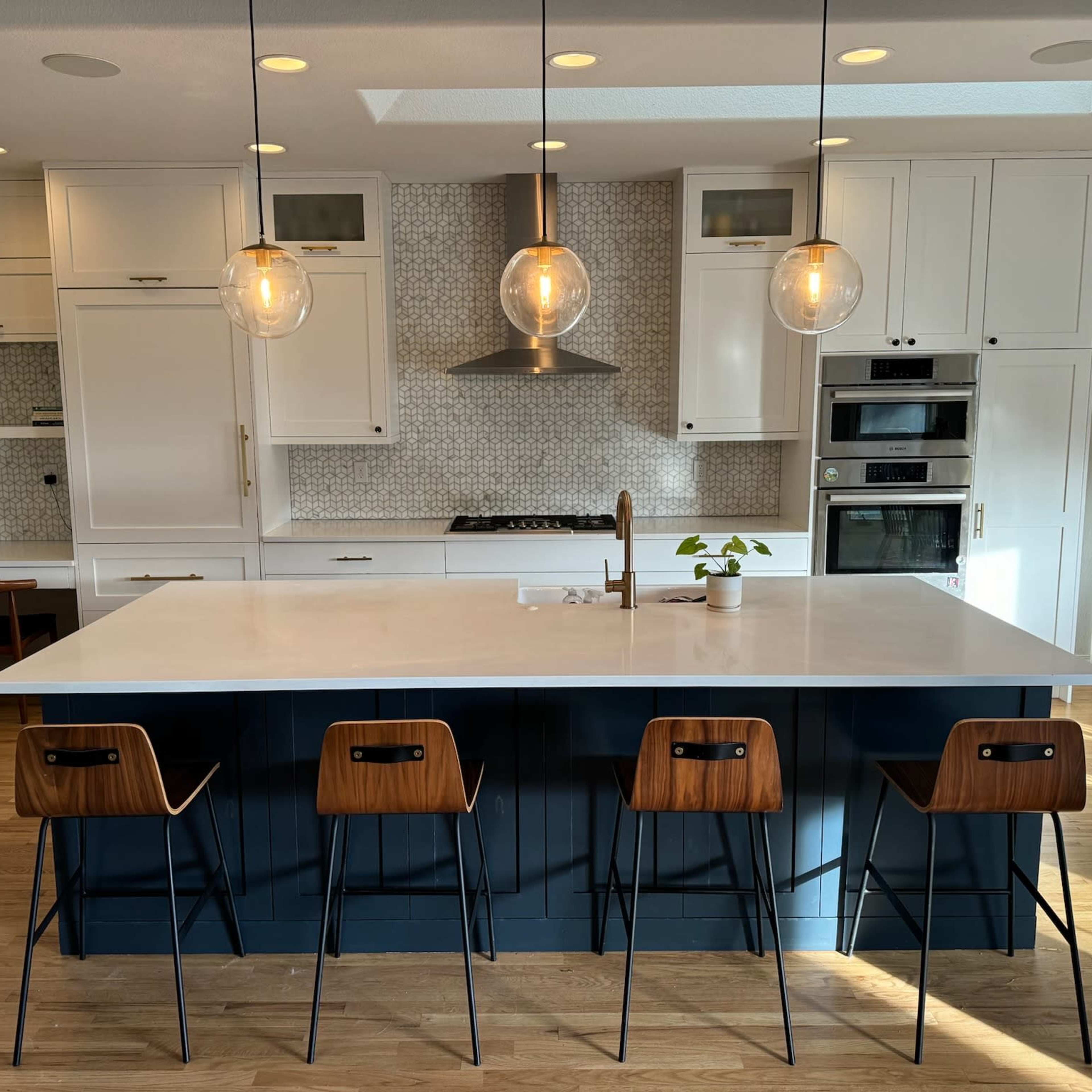 A modern kitchen featuring a large island with four bar stools, white cabinetry, and pendant lighting.