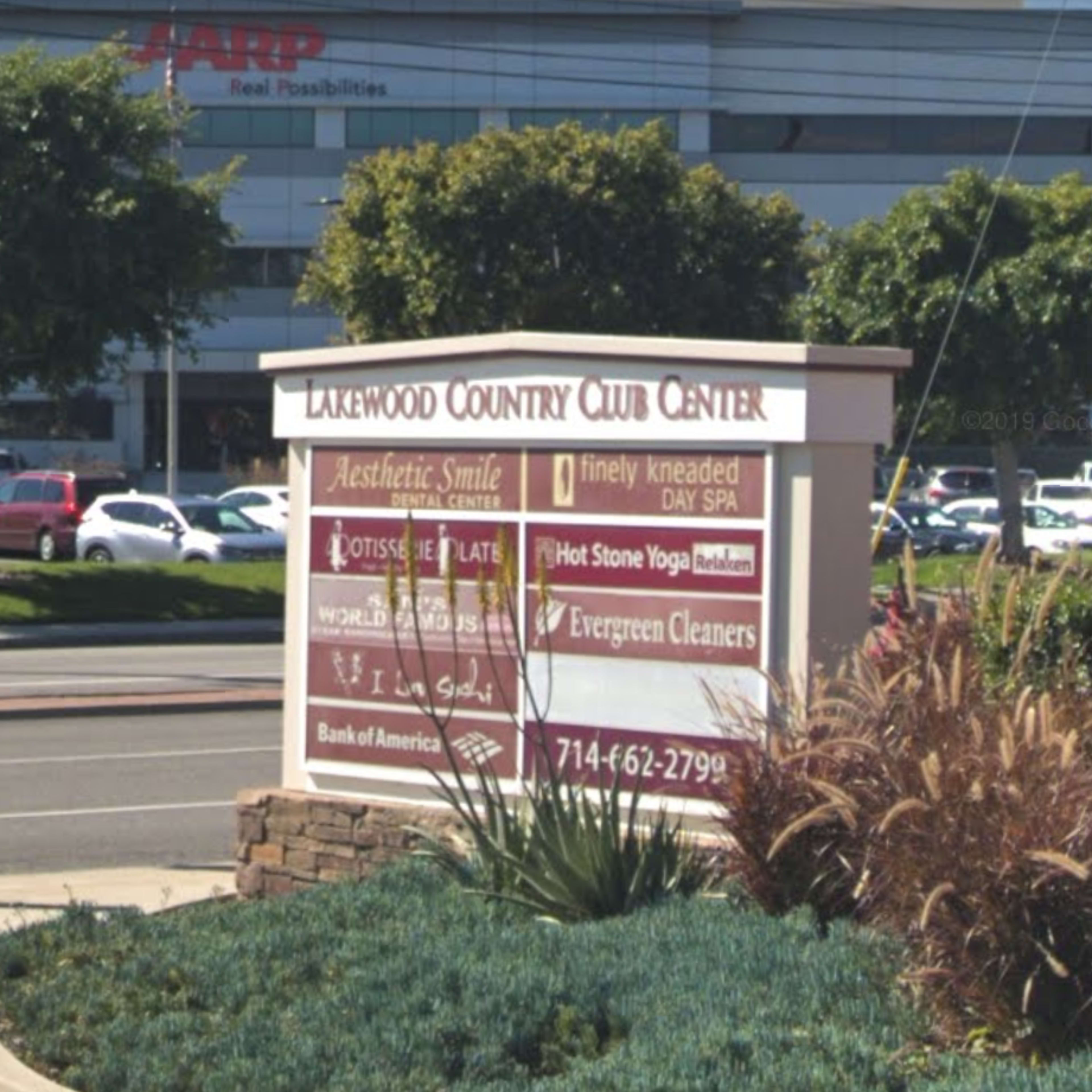 A sign for Lakewood Country Club Center listing various businesses, located at an intersection with parked cars in the background.